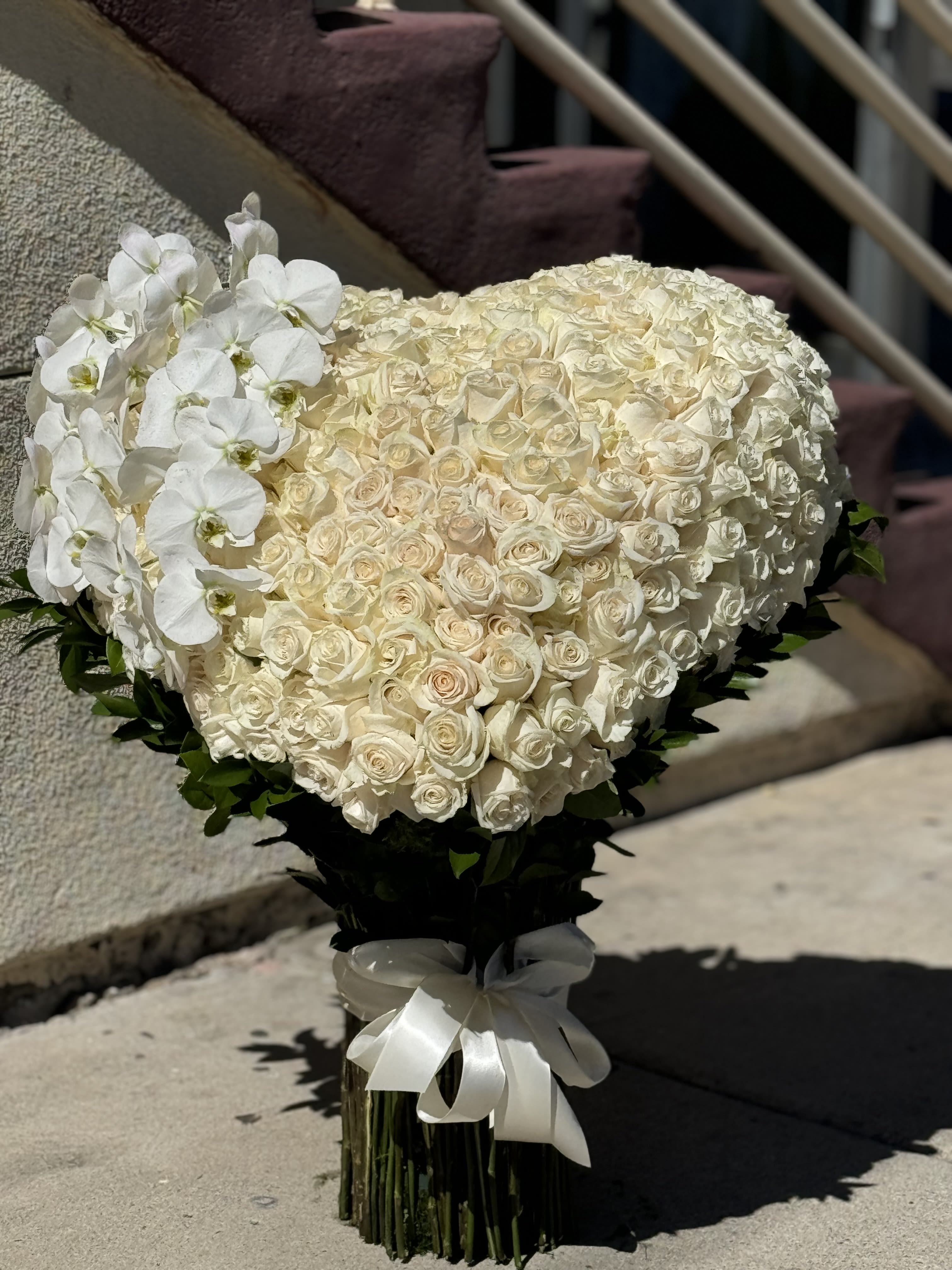 Heart-shaped bouquet of white roses with white orchids and a ribbon wrap