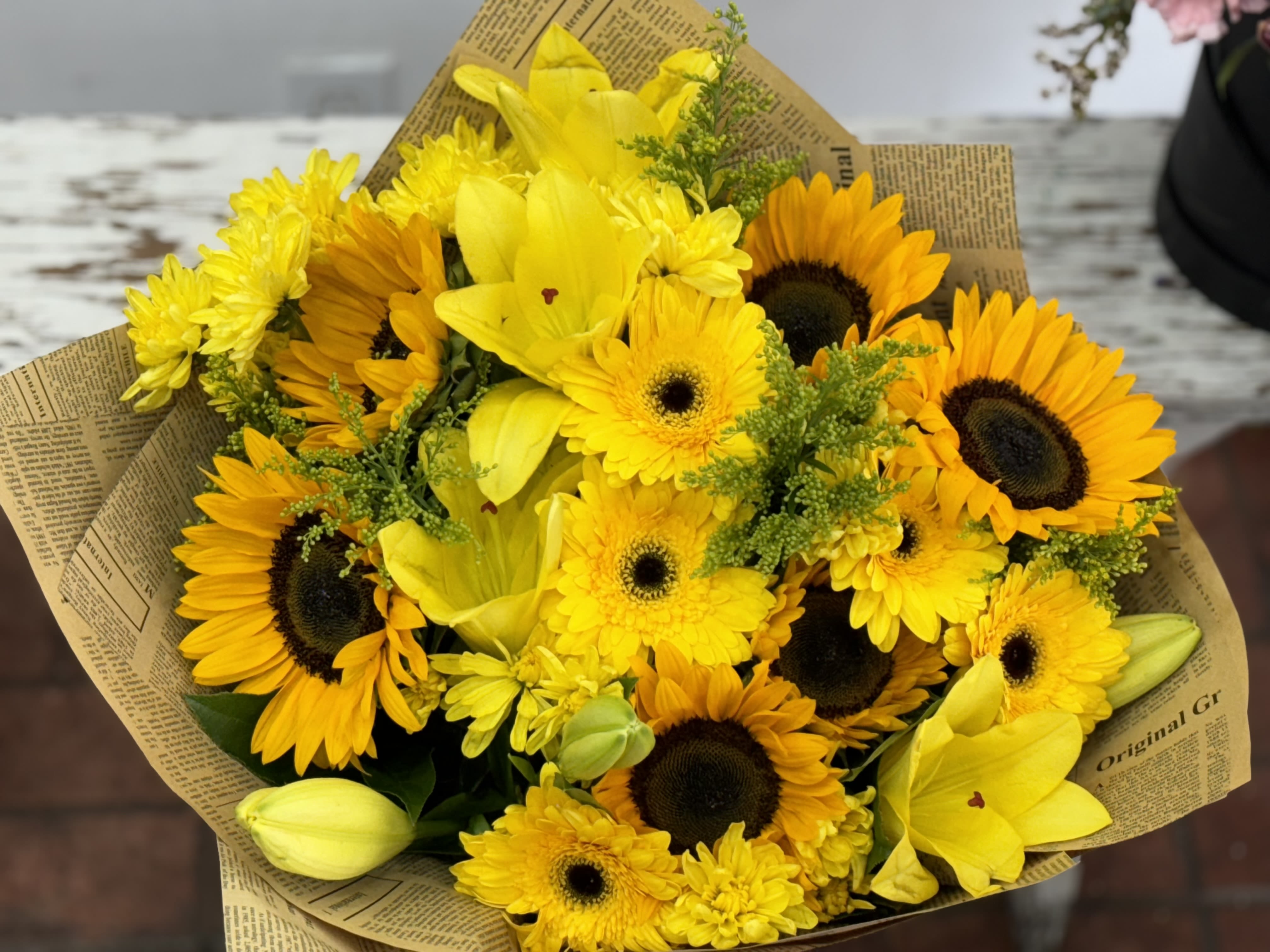 Bouquet of yellow sunflowers and lilies wrapped in newspaper-style paper