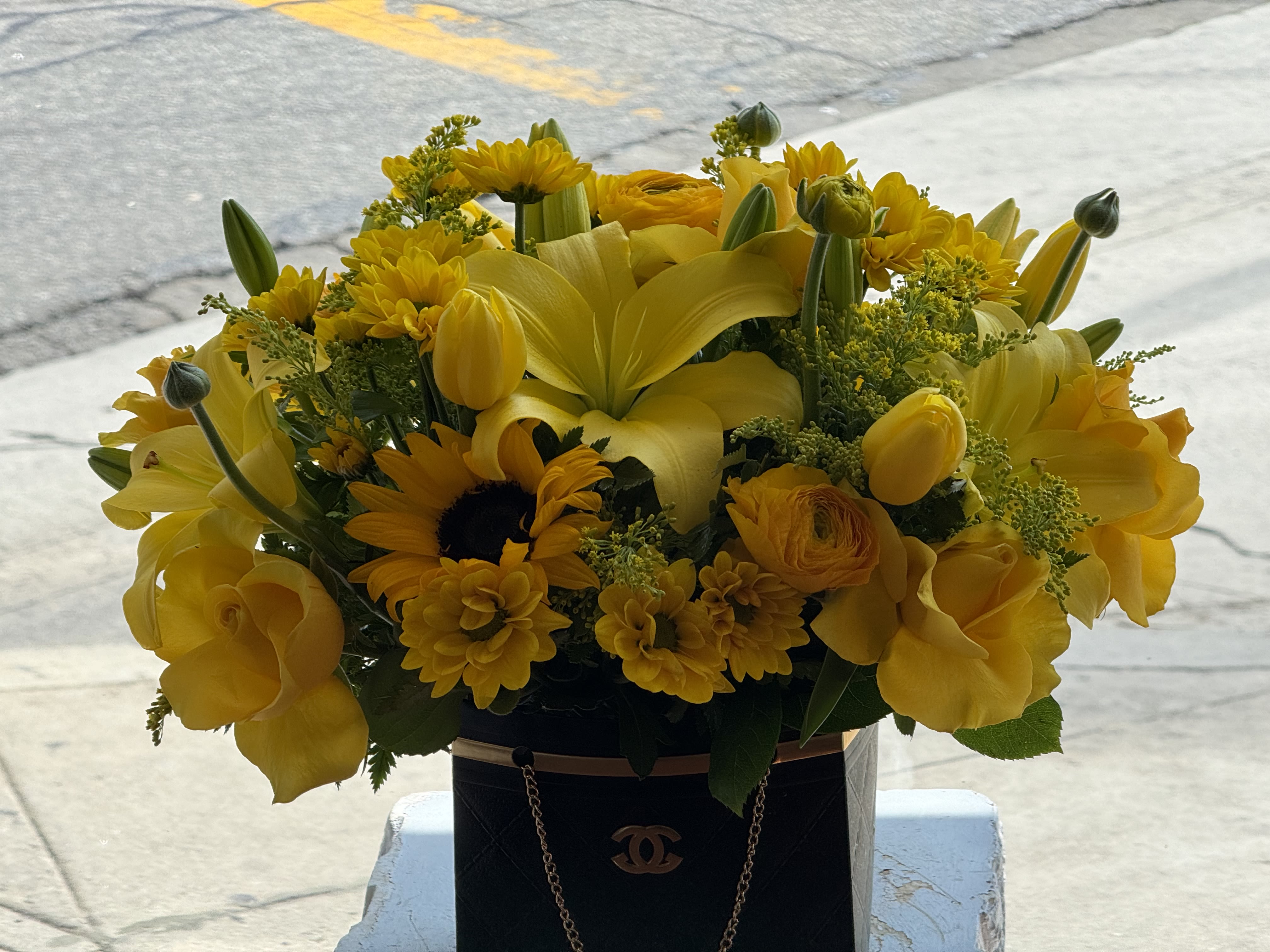 Yellow floral arrangement in a black handbag-style container