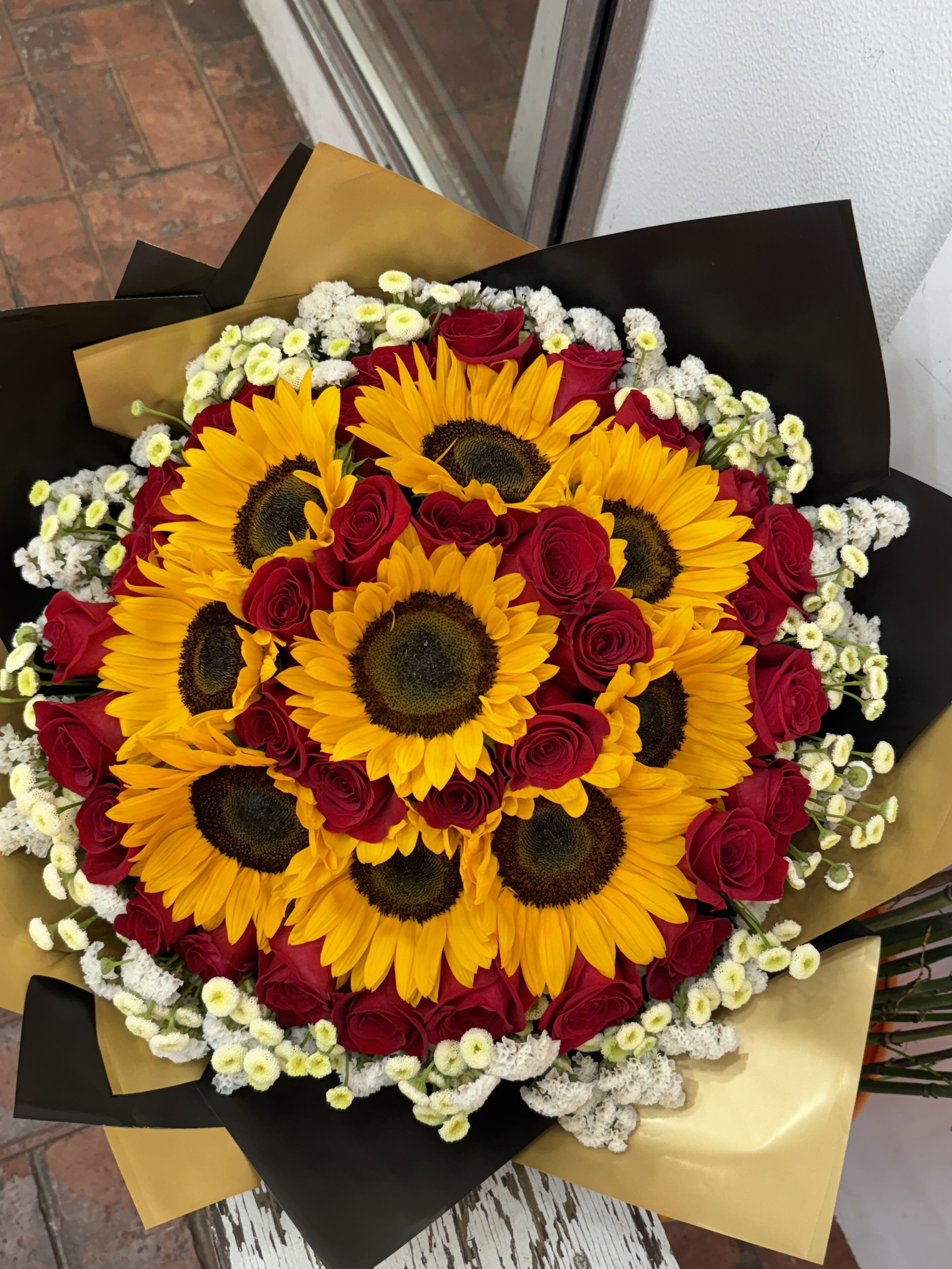 Bouquet of sunflowers and red roses wrapped in black and gold paper