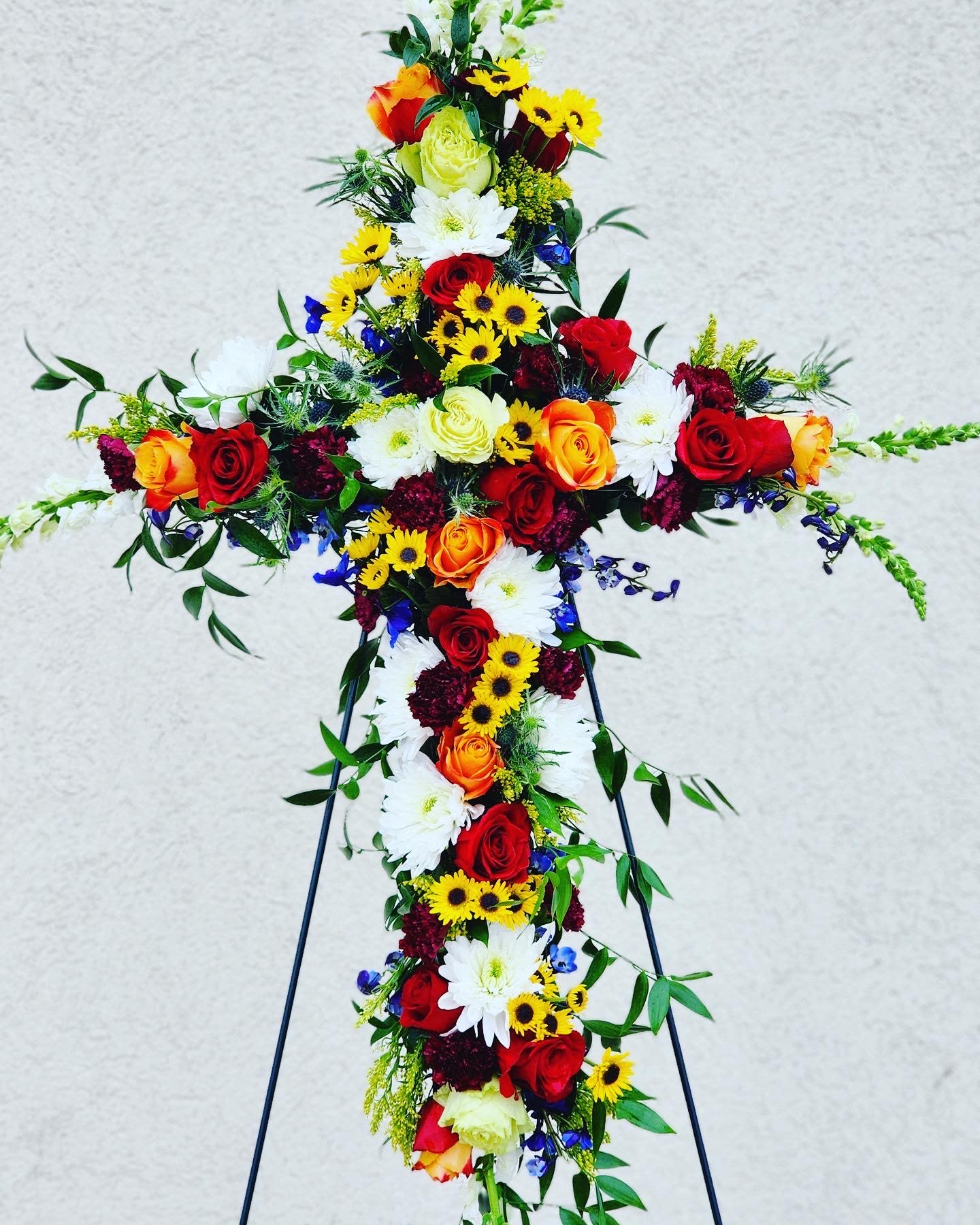 Cross-shaped floral tribute with red, orange, yellow, and white flowers