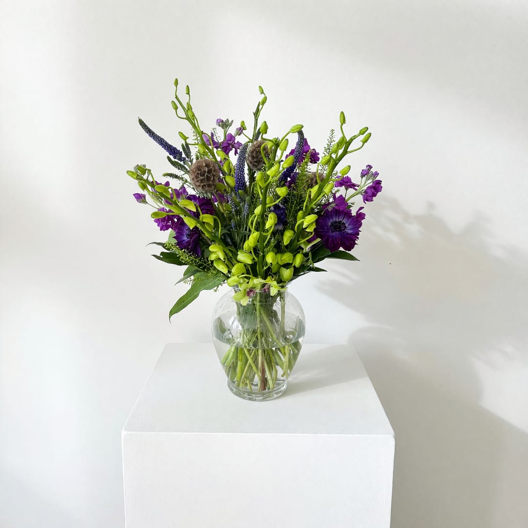 Purple and green mixed bouquet in a clear glass vase