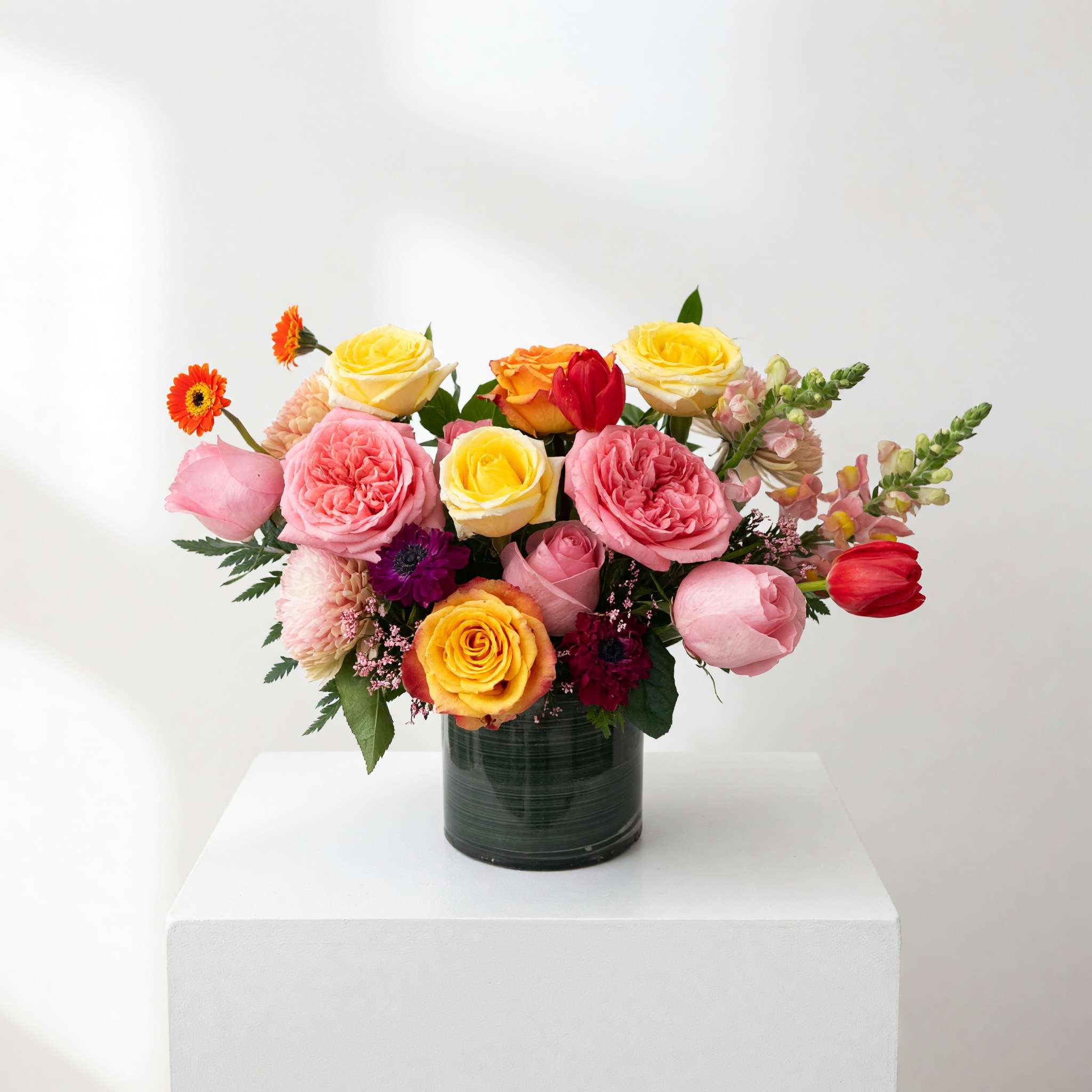 Mixed pink, yellow, and orange roses in a dark glass vase