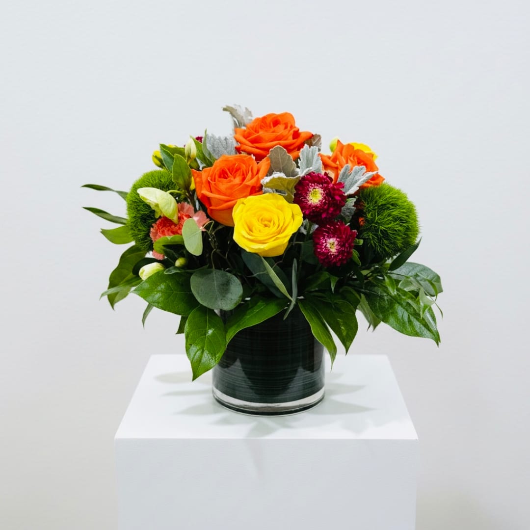Orange and yellow roses in a glass vase with green accents