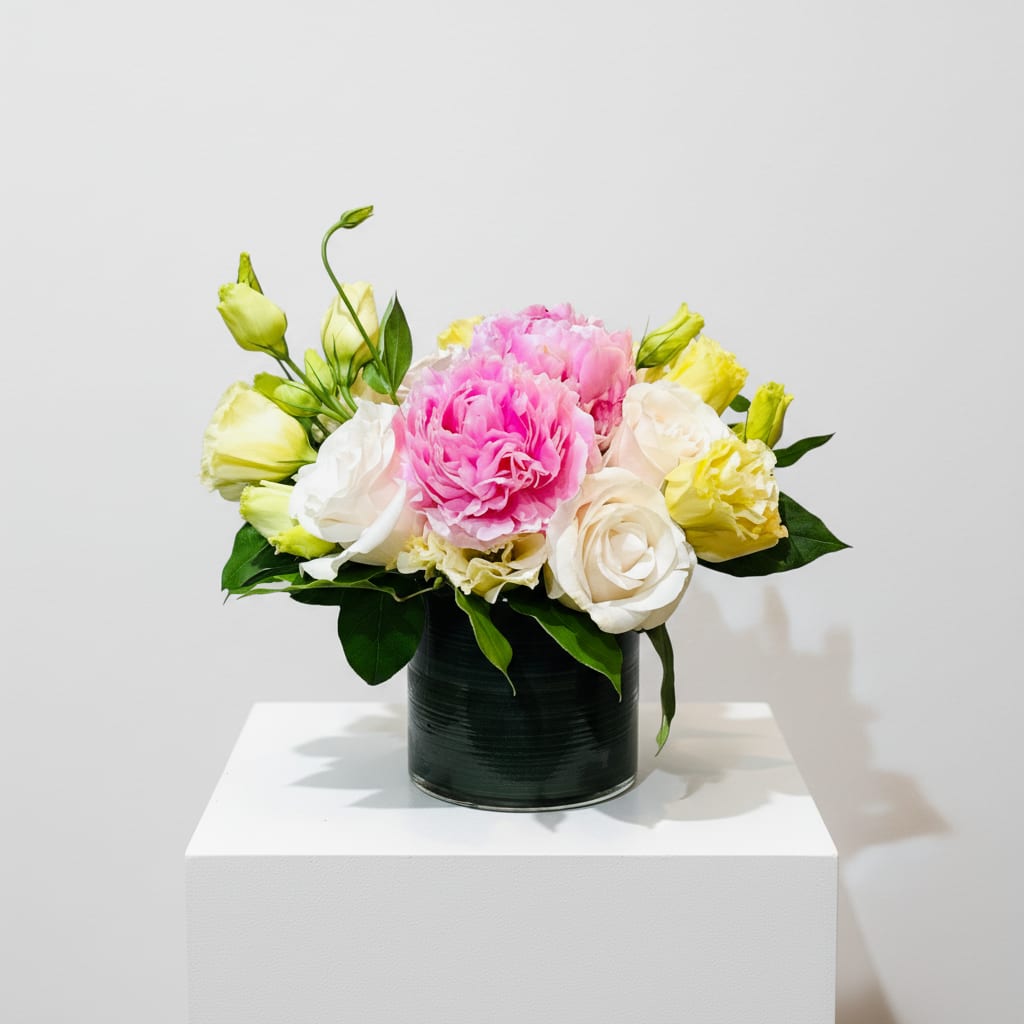 Pink and White Peony and Rose Arrangement in Glass Vase - A compact cluster of lush pink peonies takes center stage in this birthday and anniversary flower arrangement, surrounded by creamy white roses for a softly romantic look. Designed as a thinking-of-you or thank-you gift that also brightens get-well tables, the bouquet's pink and white palette reads fresh and uplifting for spring or winter moments alike. The rounded, table-ready shape makes the recipient feel genuinely seen - the kind of arrangement that says "you matter" without words.  Creamy white roses, pale yellow lisianthus, and bright red berry clusters are tightly gathered to form a tidy, low design in a clear or dark green glass cylinder vase, lending a modern, polished presence to bedside tables or dining-room centers. The mix of textures - velvety peony petals, smooth rose blooms, delicate lisianthus buds and small berries - creates visual interest and gentle movement while staying compact. Sized to sit on a table or desk, this arrangement is easy to place and enjoy in Leesburg, VA and beyond.  Perfect for Mother's Day, anniversaries, birthdays, or as a thoughtful get-well or thank-you gesture, this arrangement arrives ready to brighten a room and lift spirits. Care is simple: keep water fresh, trim stems if needed, and place out of direct heat to extend the life of the flowers so your recipient enjoys them for days.