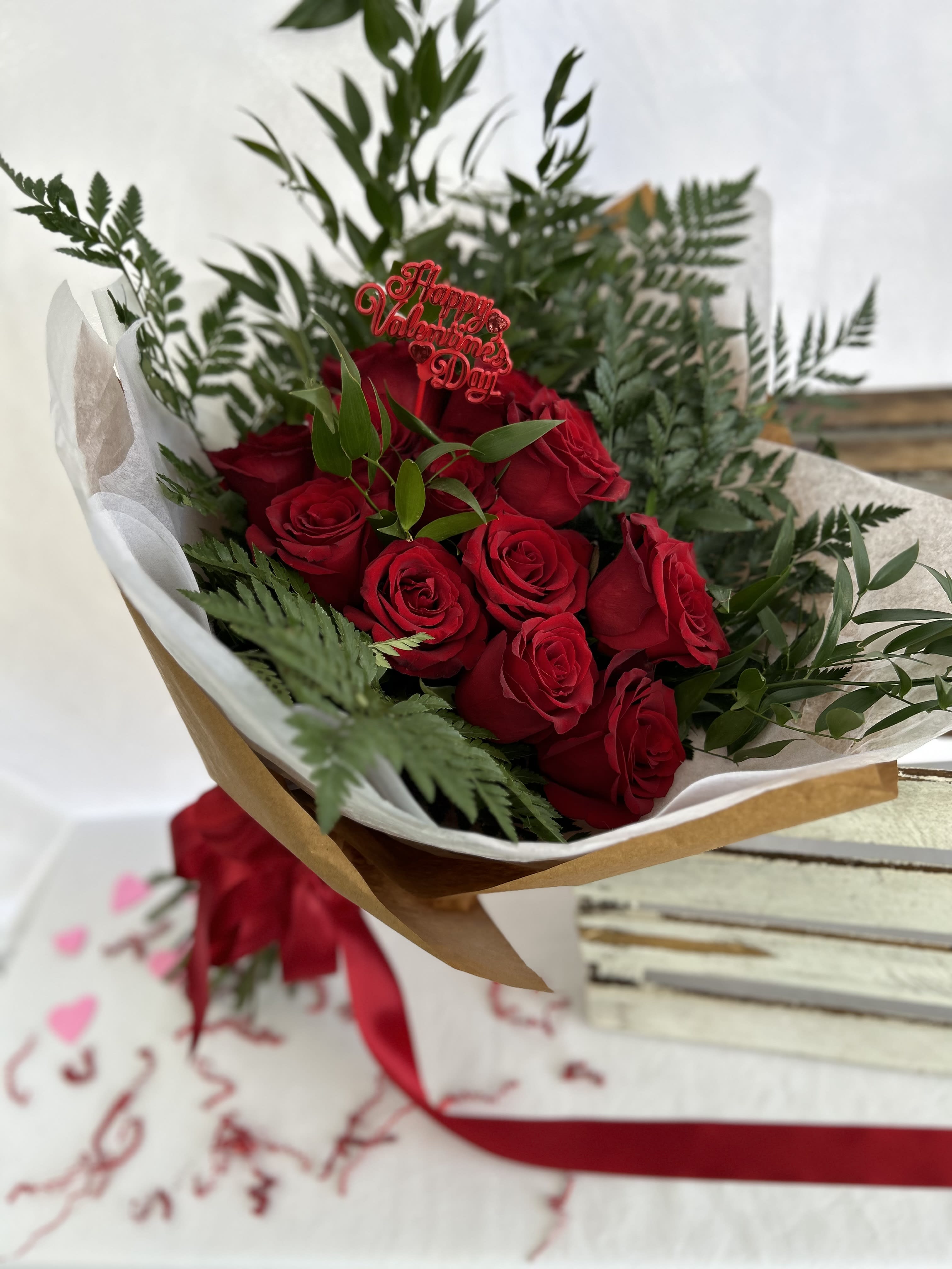 Wrapped bouquet of red roses with greenery and a Happy Valentine’s Day pick, tied with red ribbon.