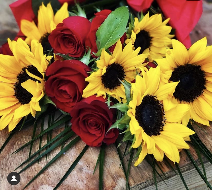 Bouquet of bright yellow sunflowers and red roses laid on a wooden surface