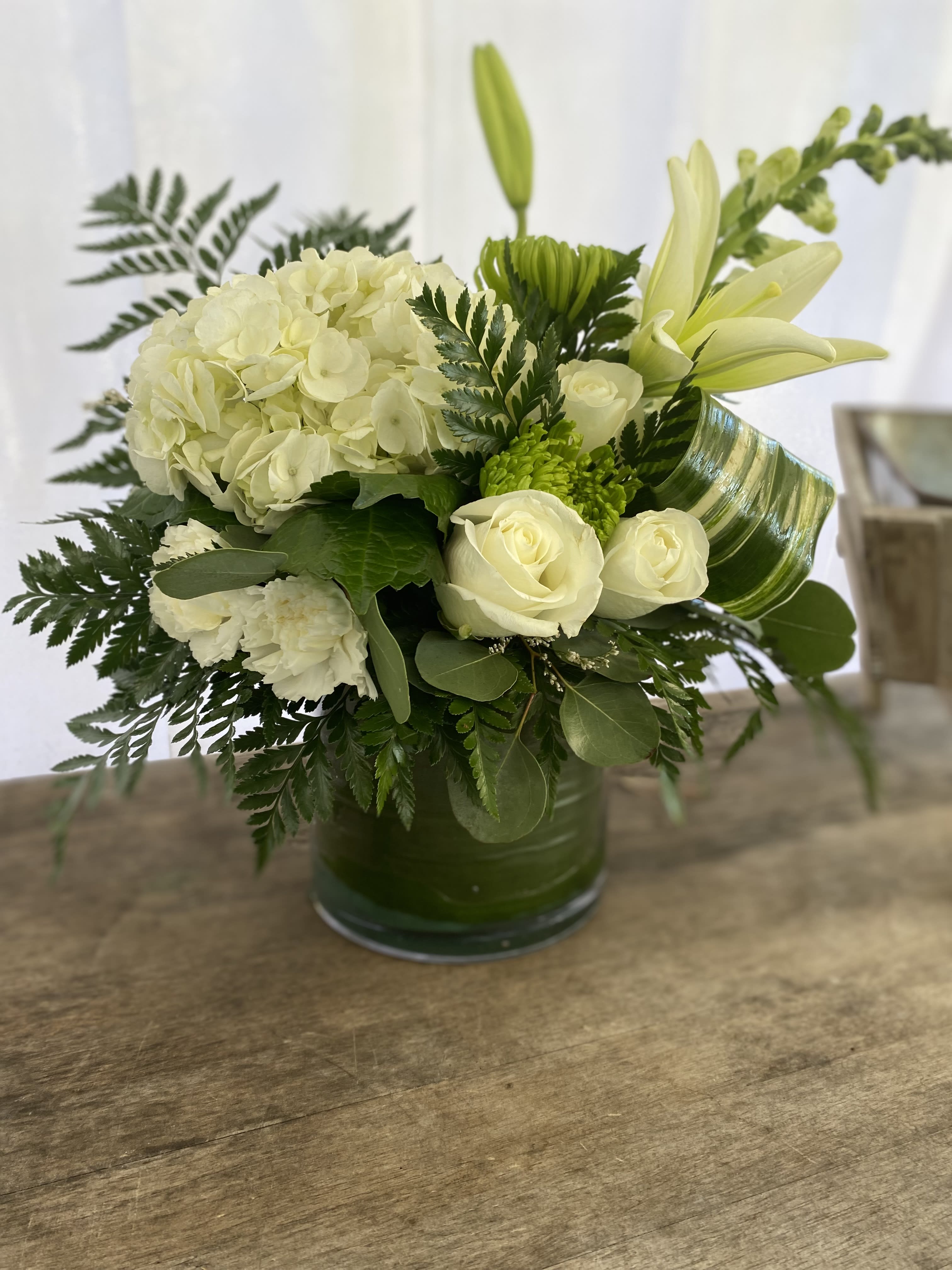 Low white and green flower arrangement with hydrangea, roses, and lilies in a green-lined glass vase