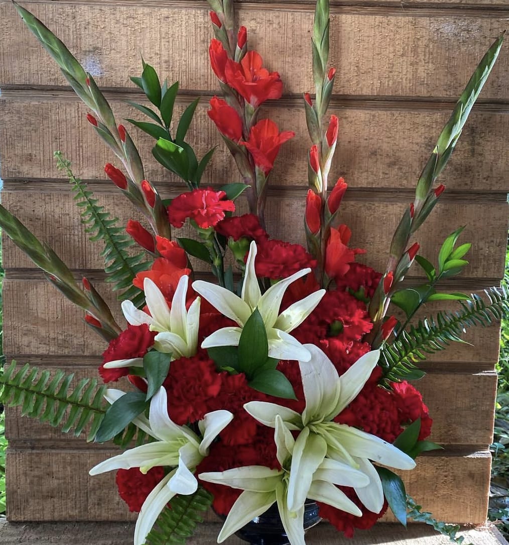 Tall red and white arrangement with lilies, carnations, and gladiolus in a black vase