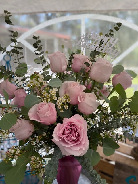 Pink rose birthday arrangement with filler flowers in a pink vase and a Happy Birthday pick.