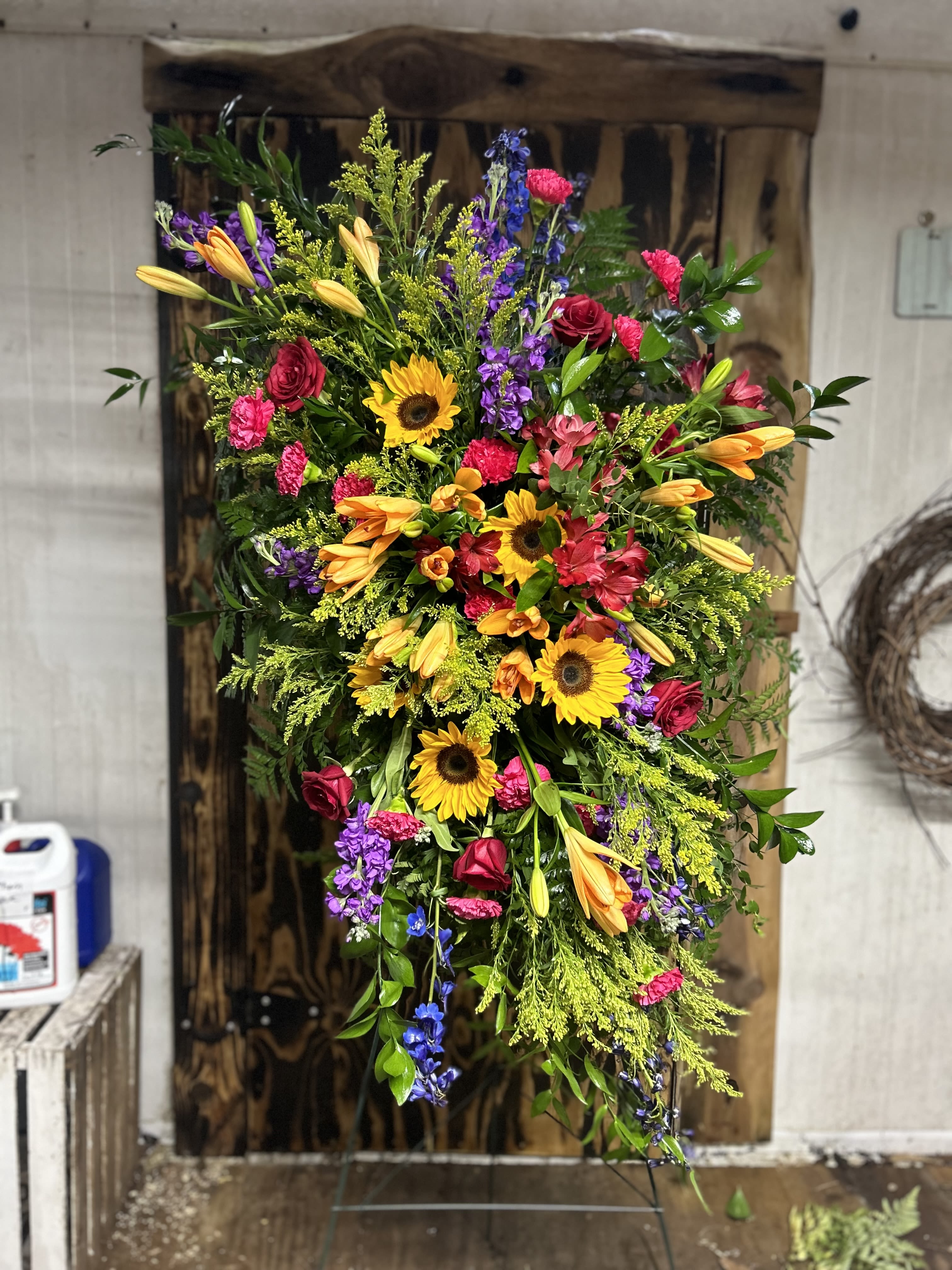 Tall standing spray of sunflowers, orange lilies, and bright mixed flowers on a metal easel.
