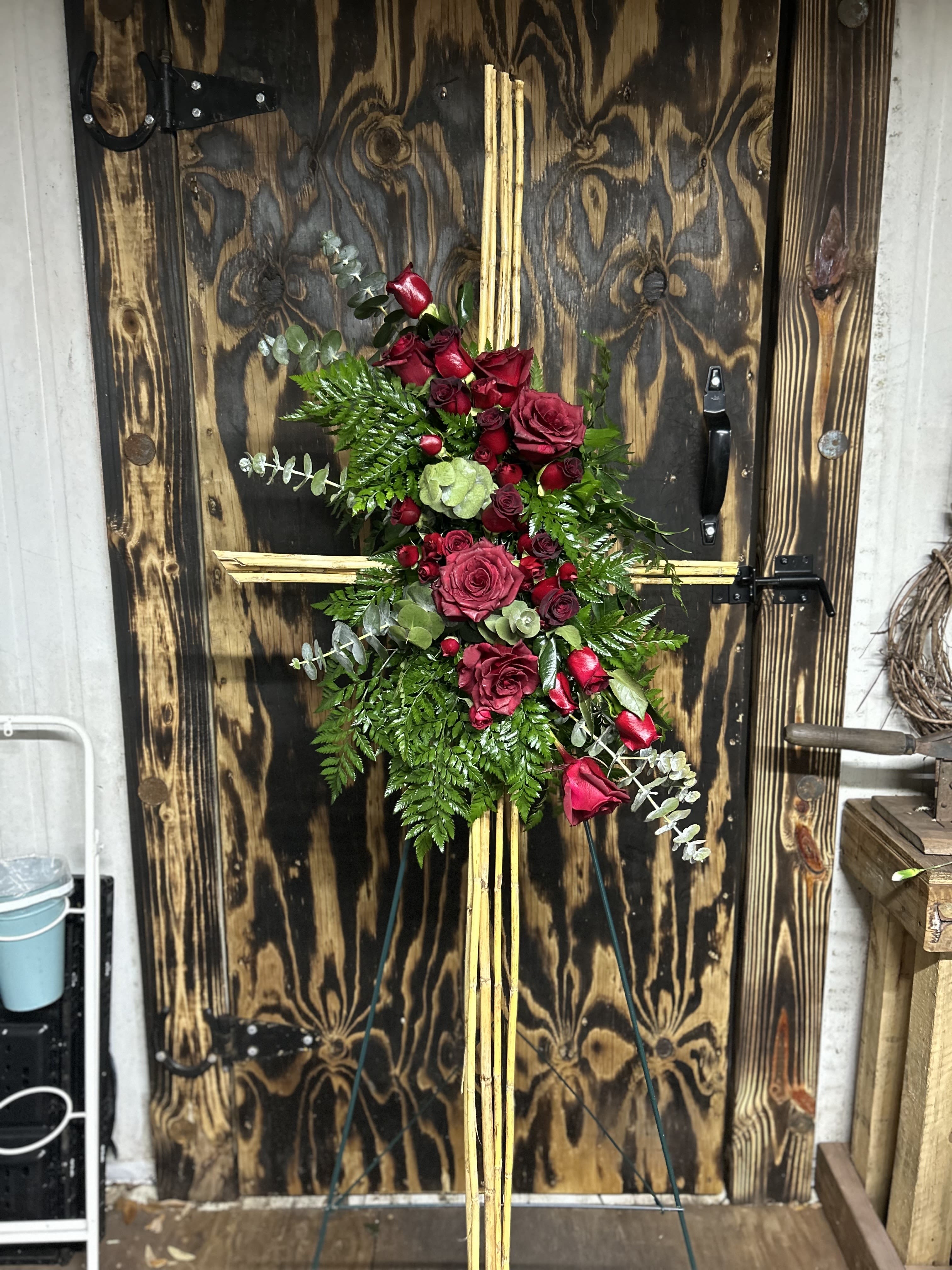 Tall cross-shaped standing spray with red roses and greenery on a wooden easel.