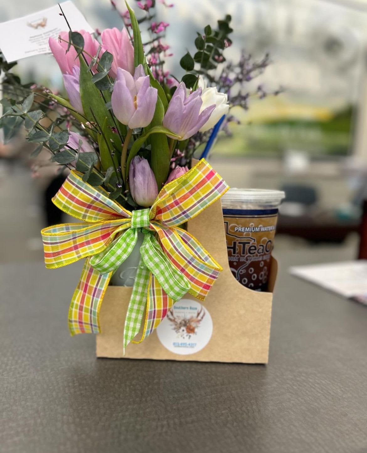 Gift caddy with pastel tulip bouquet, plaid bow, and iced tea cup on a table