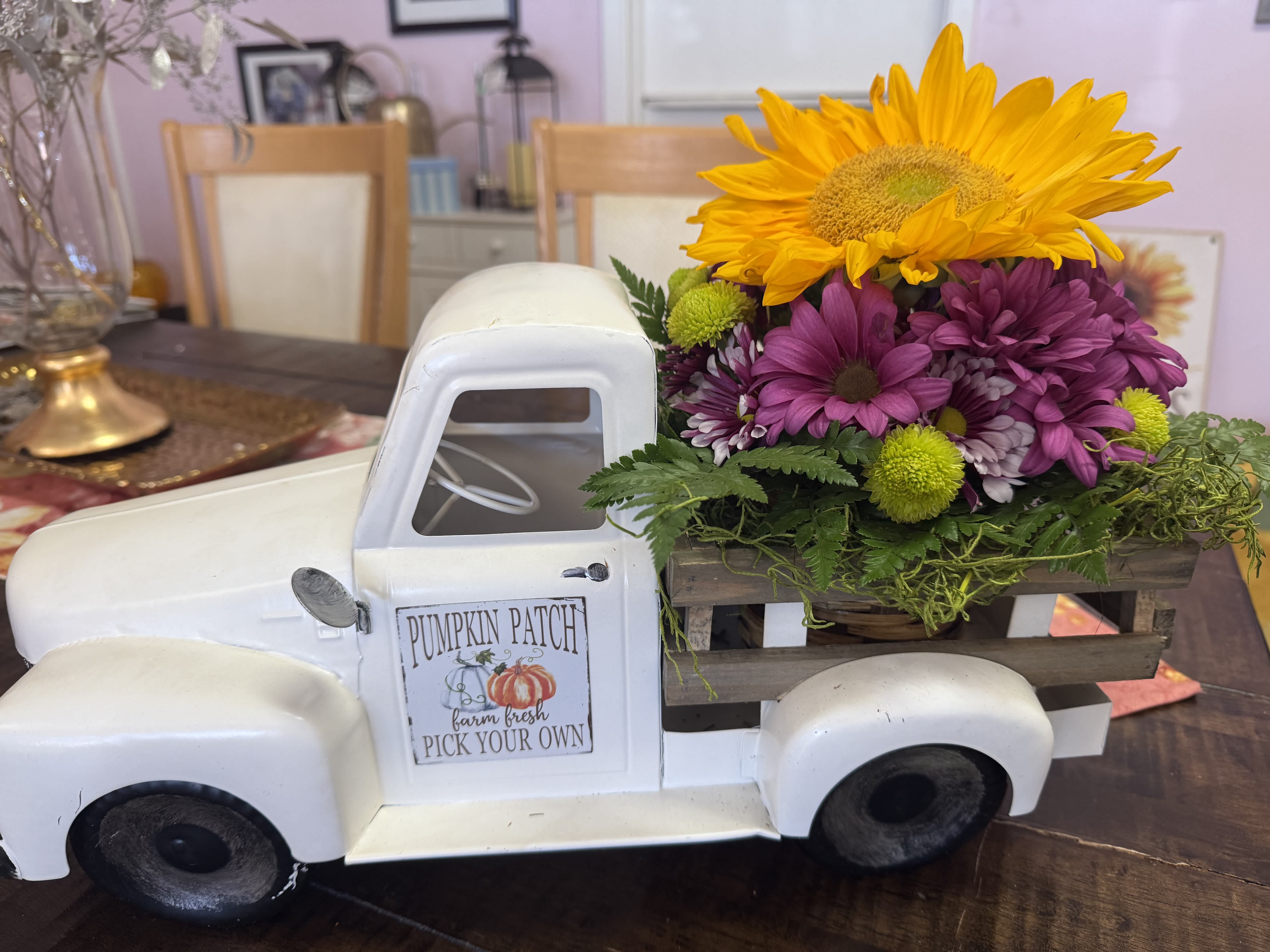 Flower arrangement in a white pickup truck planter with a sunflower and purple daisies