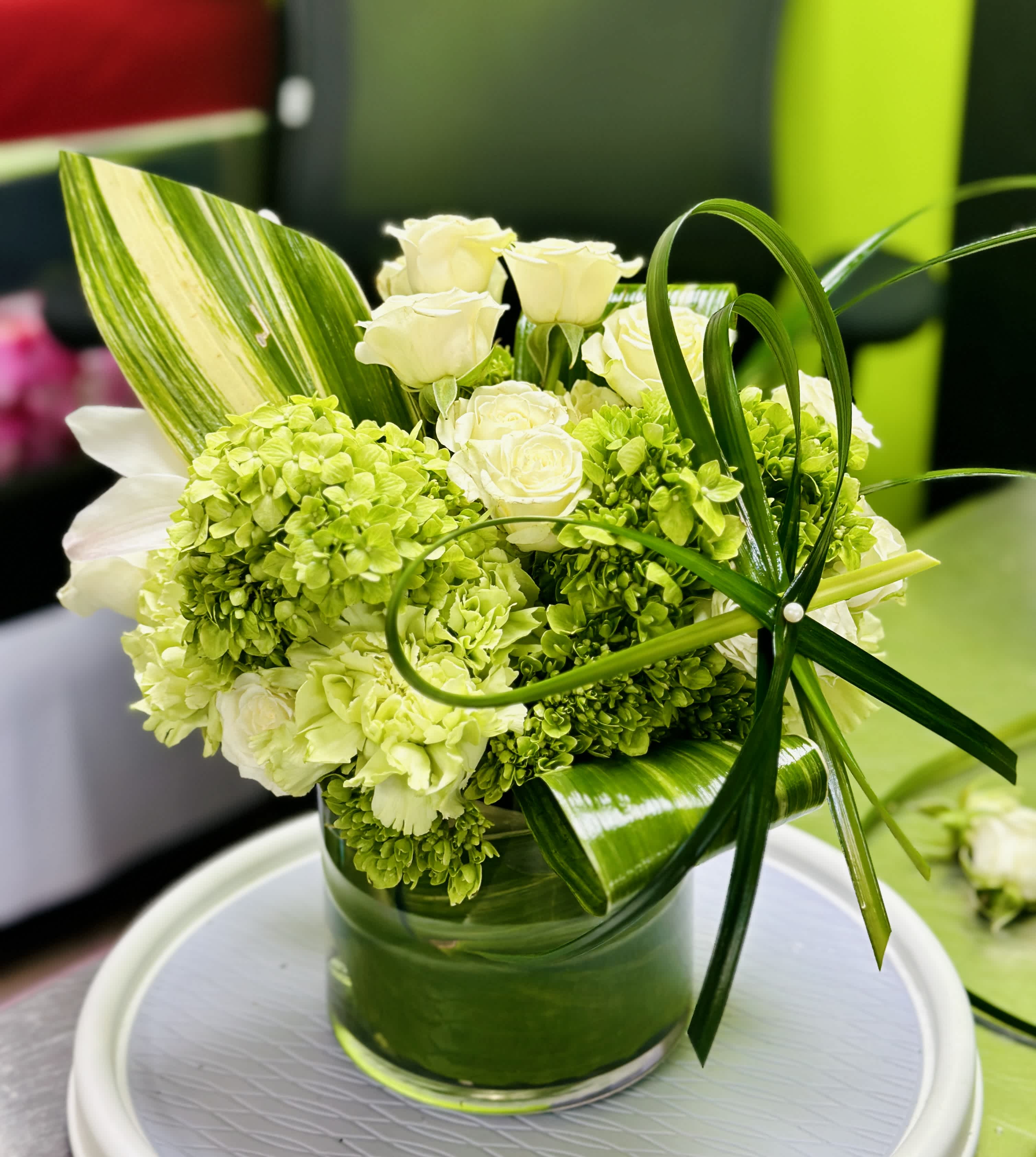 The Ashley - The Ashley is an arrangement where classy meets grand, that’s sure to bring a wow factor. Designed in a cylinder vase full of lush green &amp; white stems, with our premium size featuring orchids. 