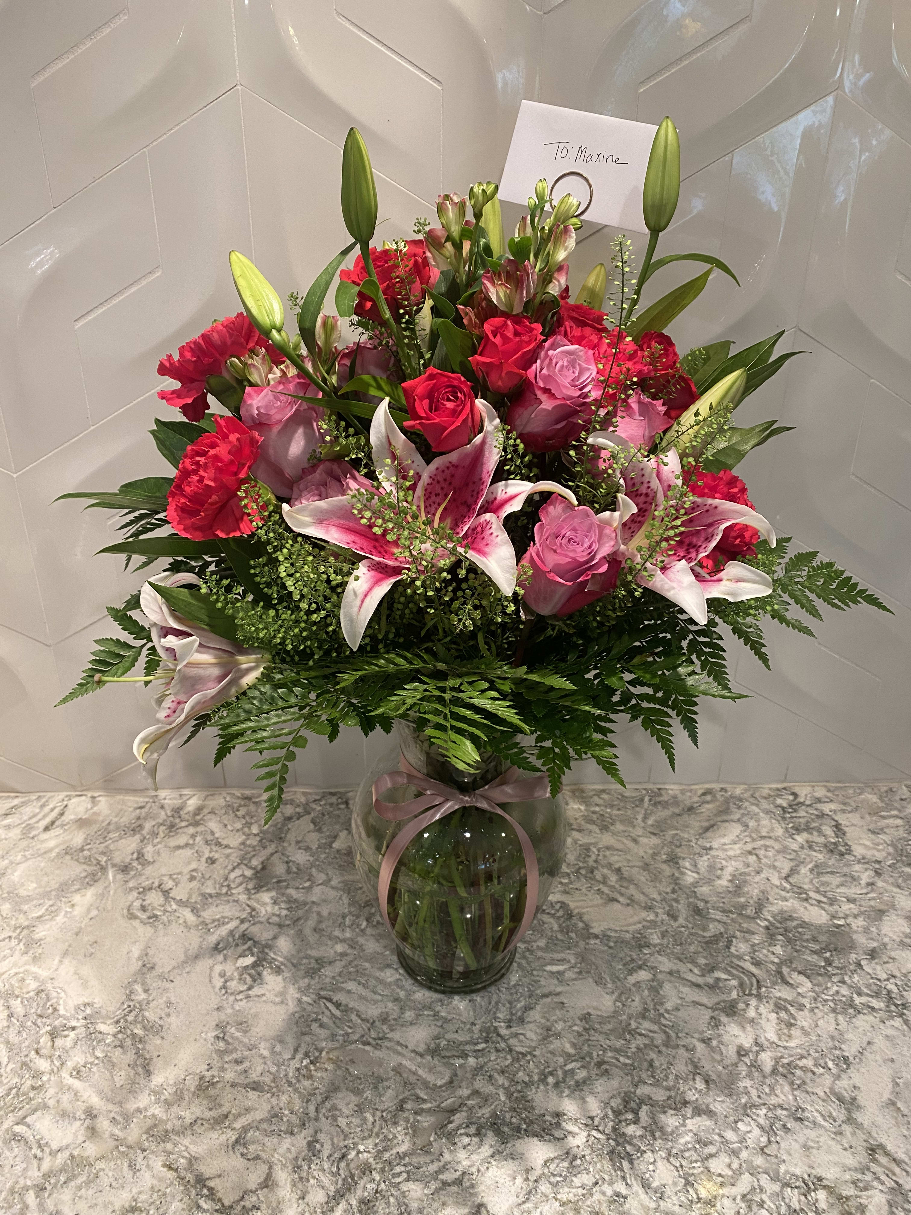 Pink roses and lilies arranged in a glass vase with a ribbon
