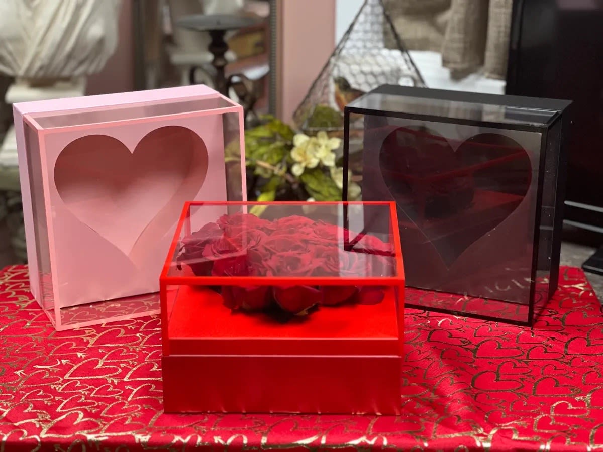 Red roses in a clear heart-shaped box with pink and black heart boxes nearby