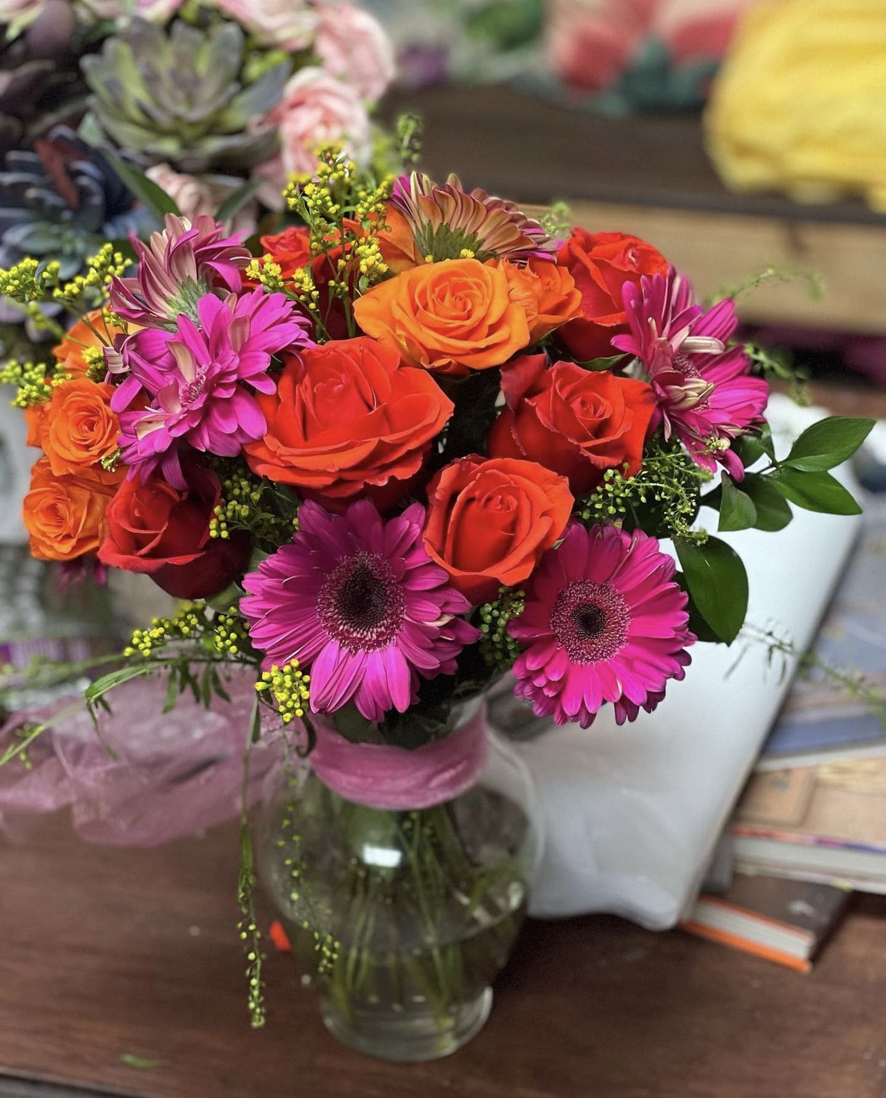 Bouquet of orange and red roses with pink daisies in a glass vase