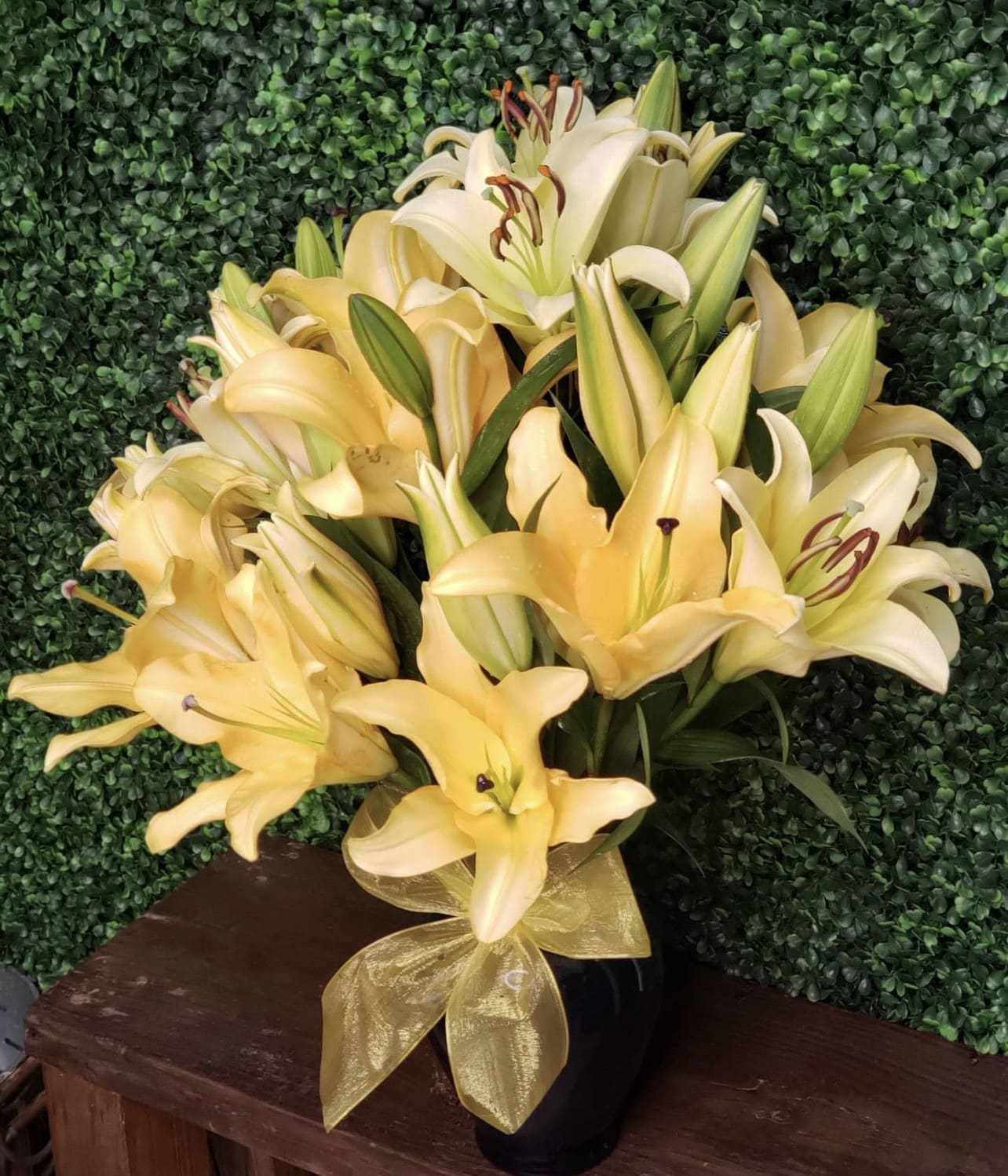Bouquet of pale yellow lilies in a black vase with a gold ribbon