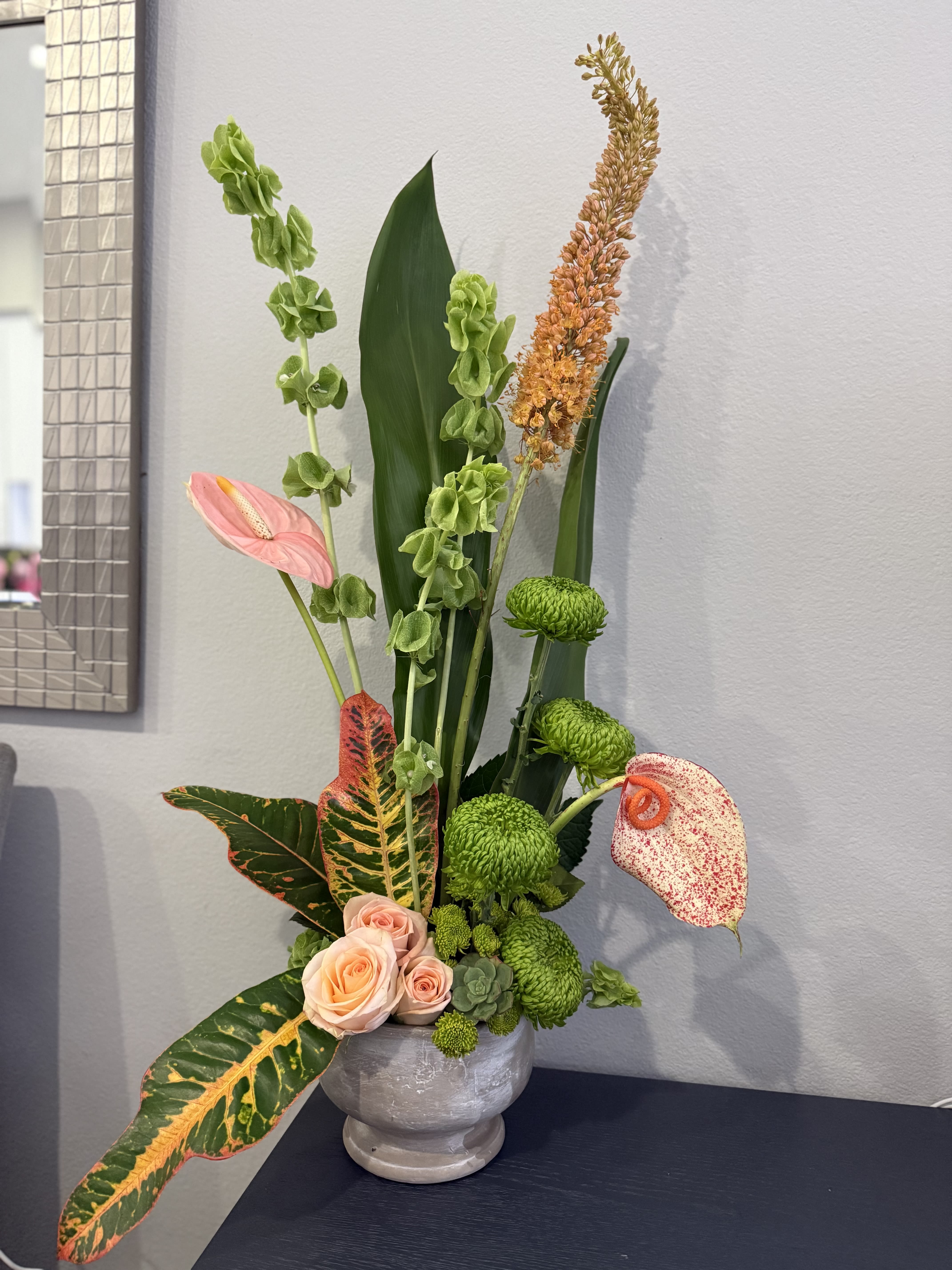 Tall tropical floral arrangement with pink anthuriums and green chrysanthemums in a gray vase