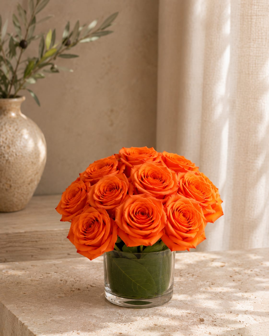 Touch of tangerine  - A compact dome of vivid orange roses arranged in a clear glass vase makes a bold, cheerful statement - perfect as a birthday bouquet, a romantic anniversary surprise, or a bright "thinking of you" gift. The warm, saturated orange tones read energetic and celebratory so the person you're sending it to will feel noticed and joyfully singled out.  Tightly gathered roses form a polished, rounded silhouette accented by fresh green foliage and touches of white for contrast. The low, clear glass vase keeps the look modern and easy to place on a dining table or desk; the arrangement reads fresh in natural light and fits well in small- to medium-sized spaces. For best enjoyment, keep the water fresh and trim stems every few days to prolong bloom life.