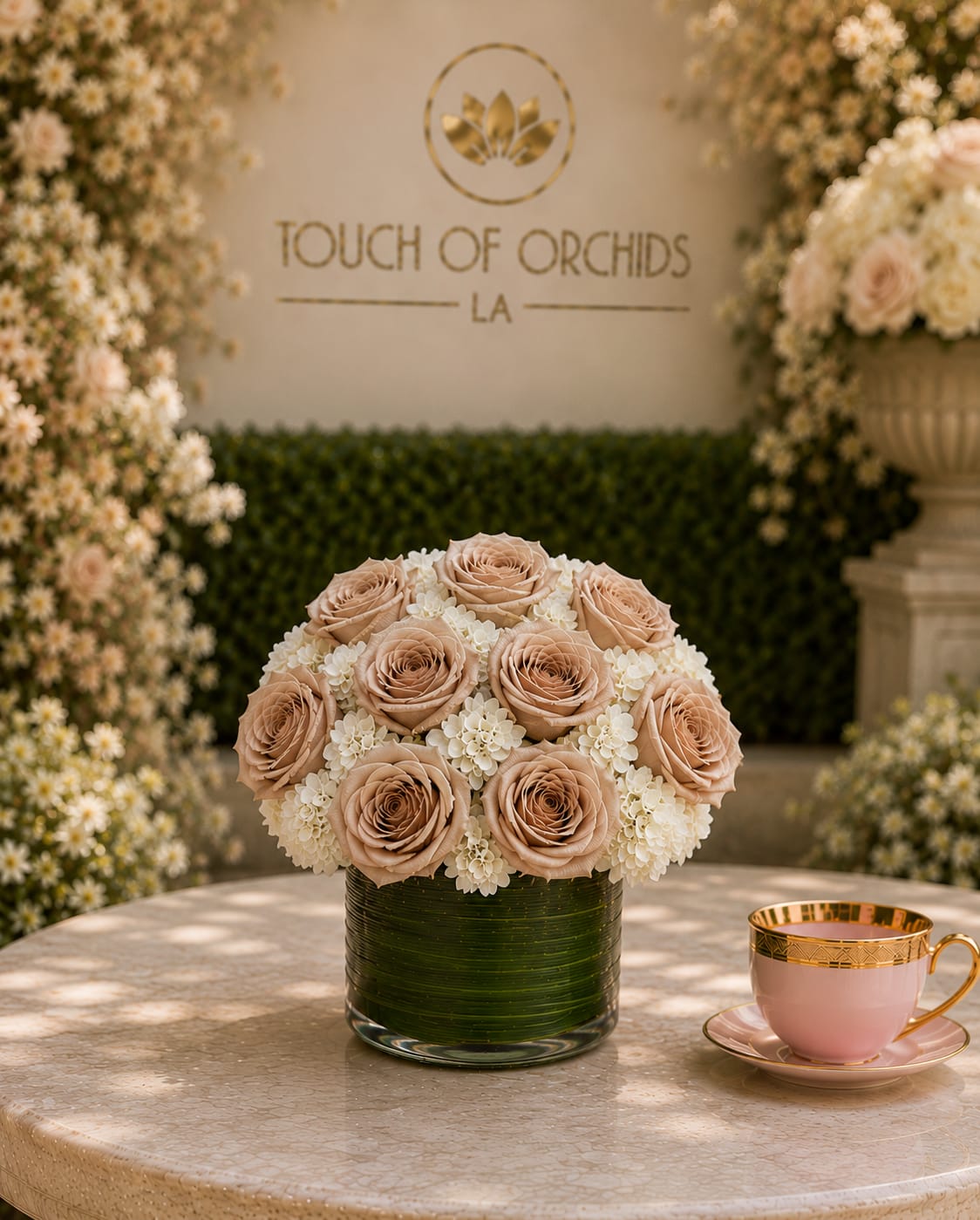 Touch of Latte - A compact cluster of blush roses and delicate white filler blooms creates a soft, romantic centerpiece perfect for a birthday bouquet, anniversary roses, or a wedding-friendly gift. The rounded, low arrangement reads intimate and refined-she'll feel genuinely celebrated by the gentle pastel palette of pink, white, and fresh green accents.  Flowers are densely arranged in a low green glass vase that gives the piece a polished, formal look and makes it easy to place on a dining table, bedside, or desk. Soft-textured rose petals and tiny white blooms form a cohesive, tactile mix; the arrangement's modest scale and sturdy glass vessel mean simple care-fresh water and a cool spot will keep it looking lovely for days-making it an elegant everyday floral gift.