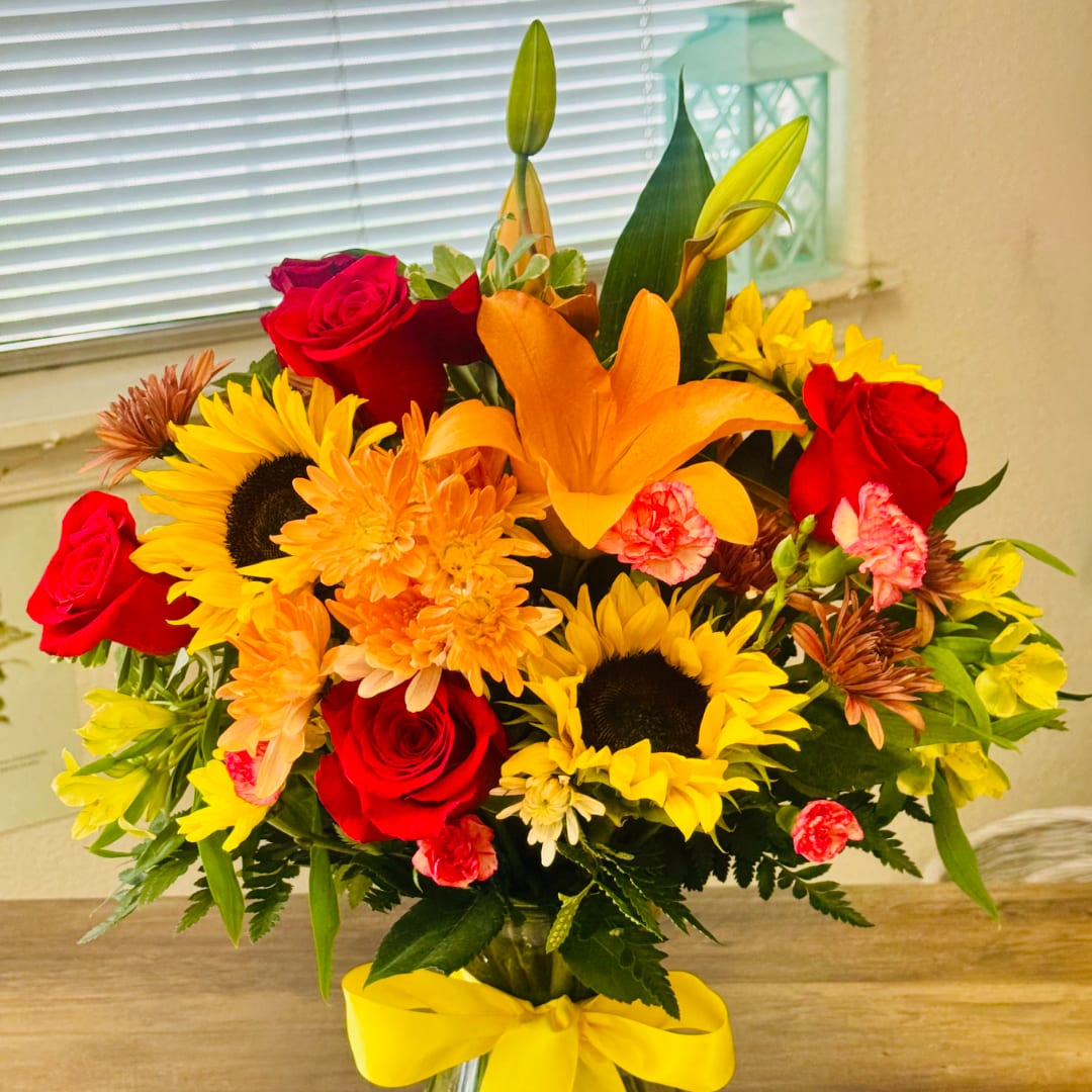 Bouquet of red roses, sunflowers, and orange lilies in a vase with a yellow ribbon