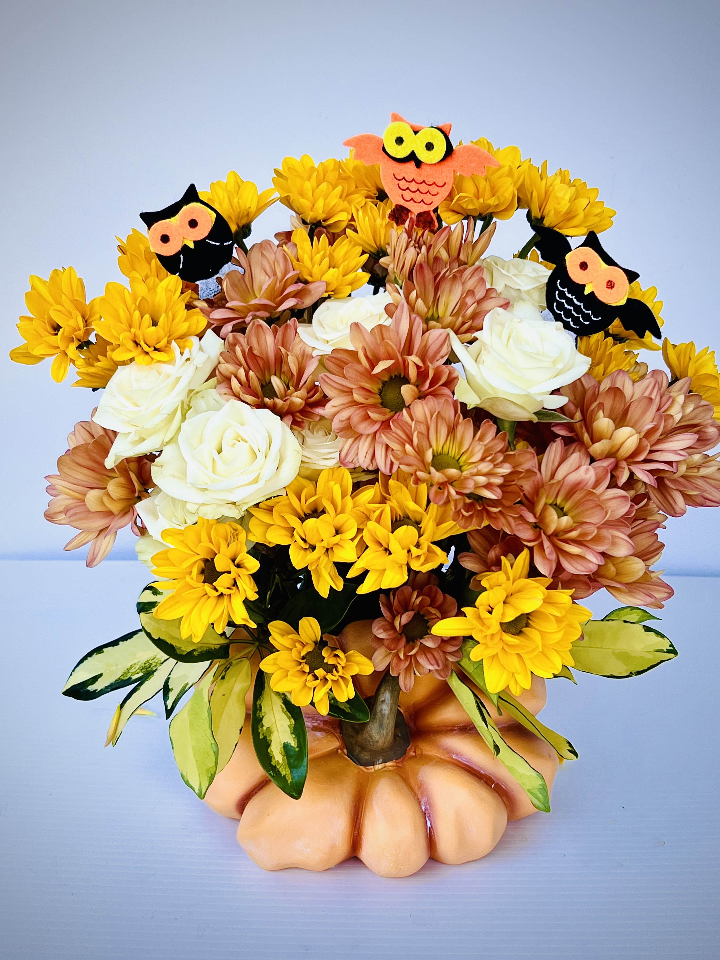Bouquet of yellow and peach flowers in a pumpkin vase with owl picks