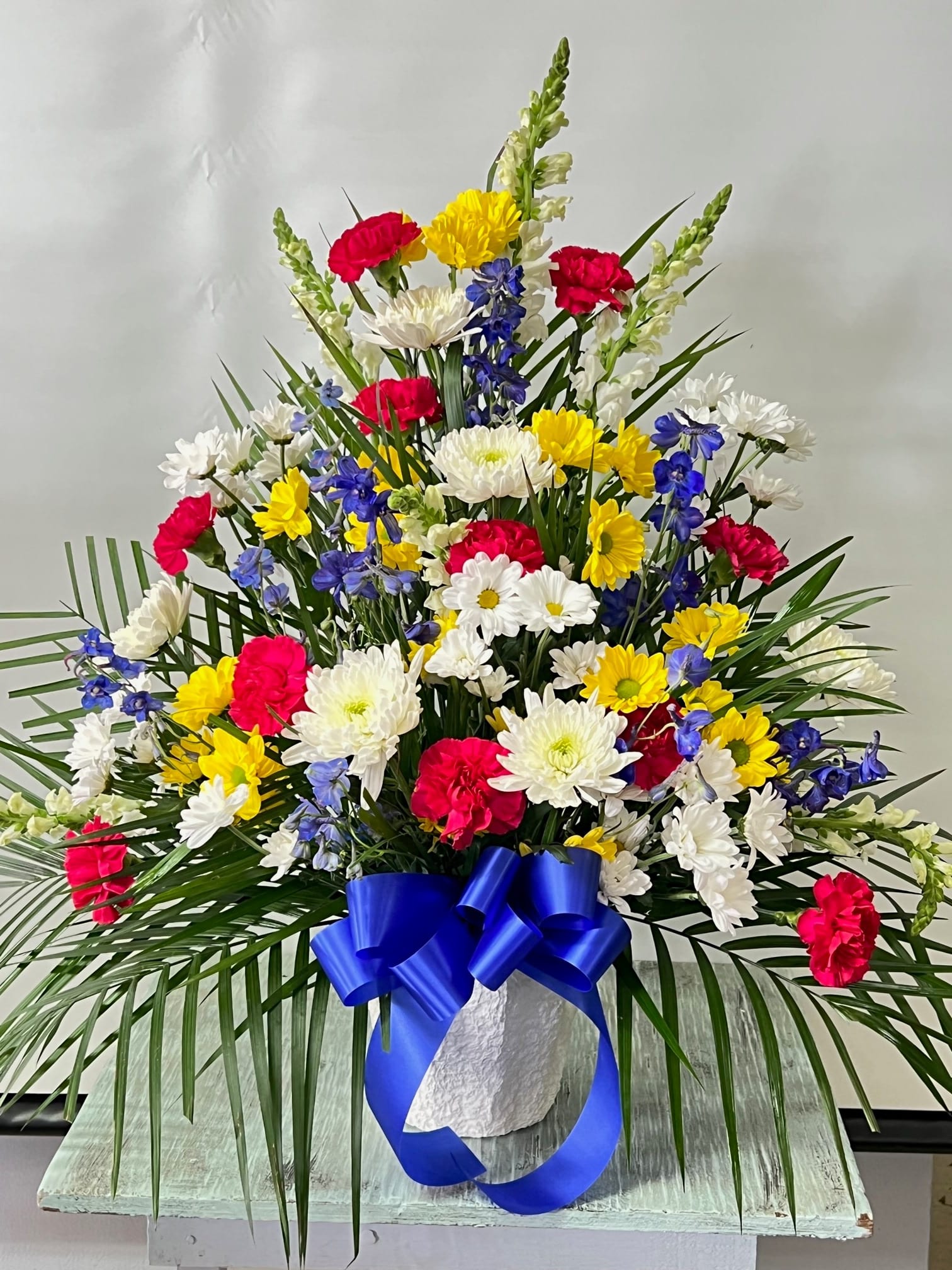 Colorful mixed flower arrangement in a white vase with a blue ribbon
