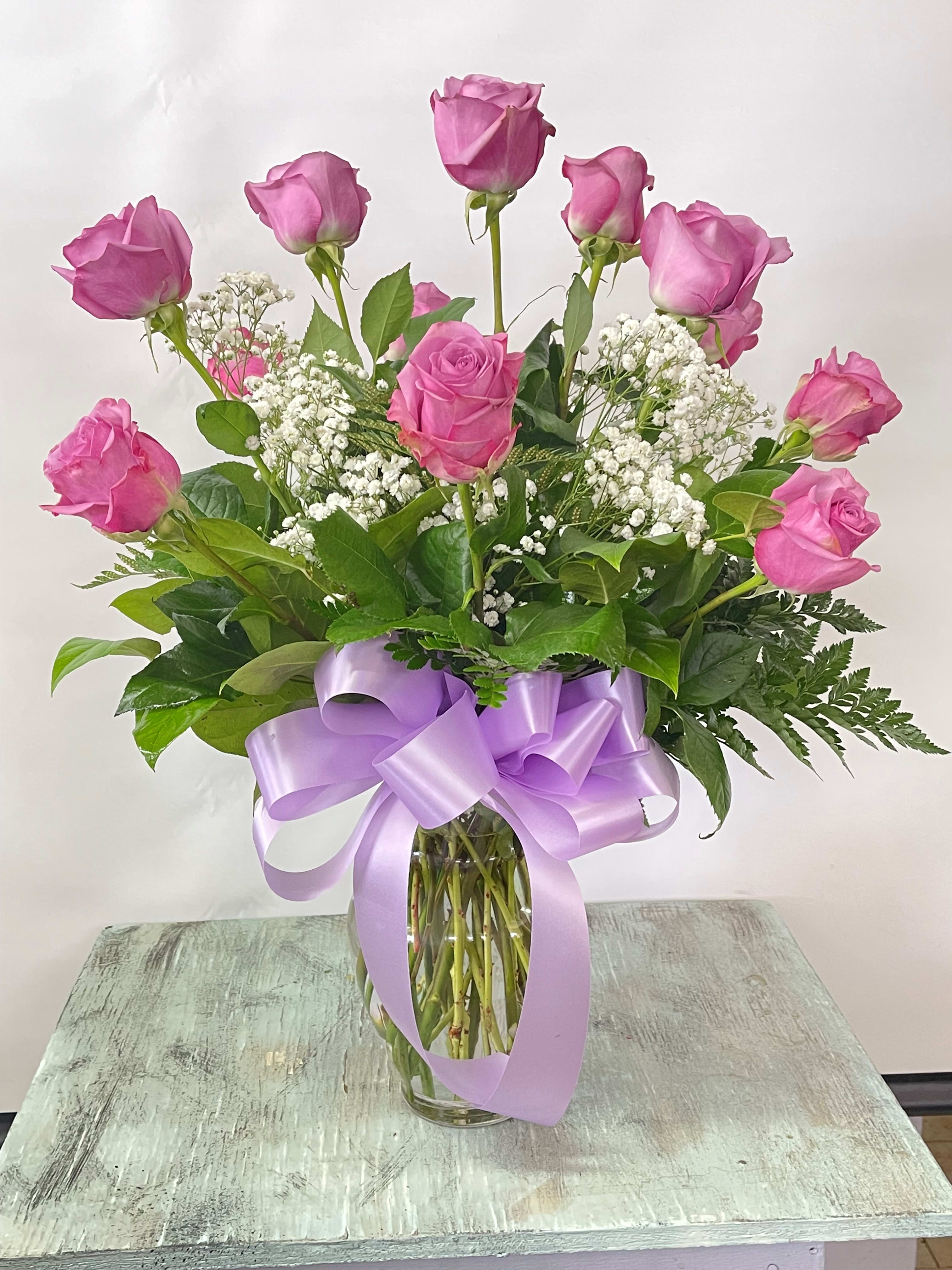 Pink roses in a glass vase with white baby's breath and a lavender ribbon