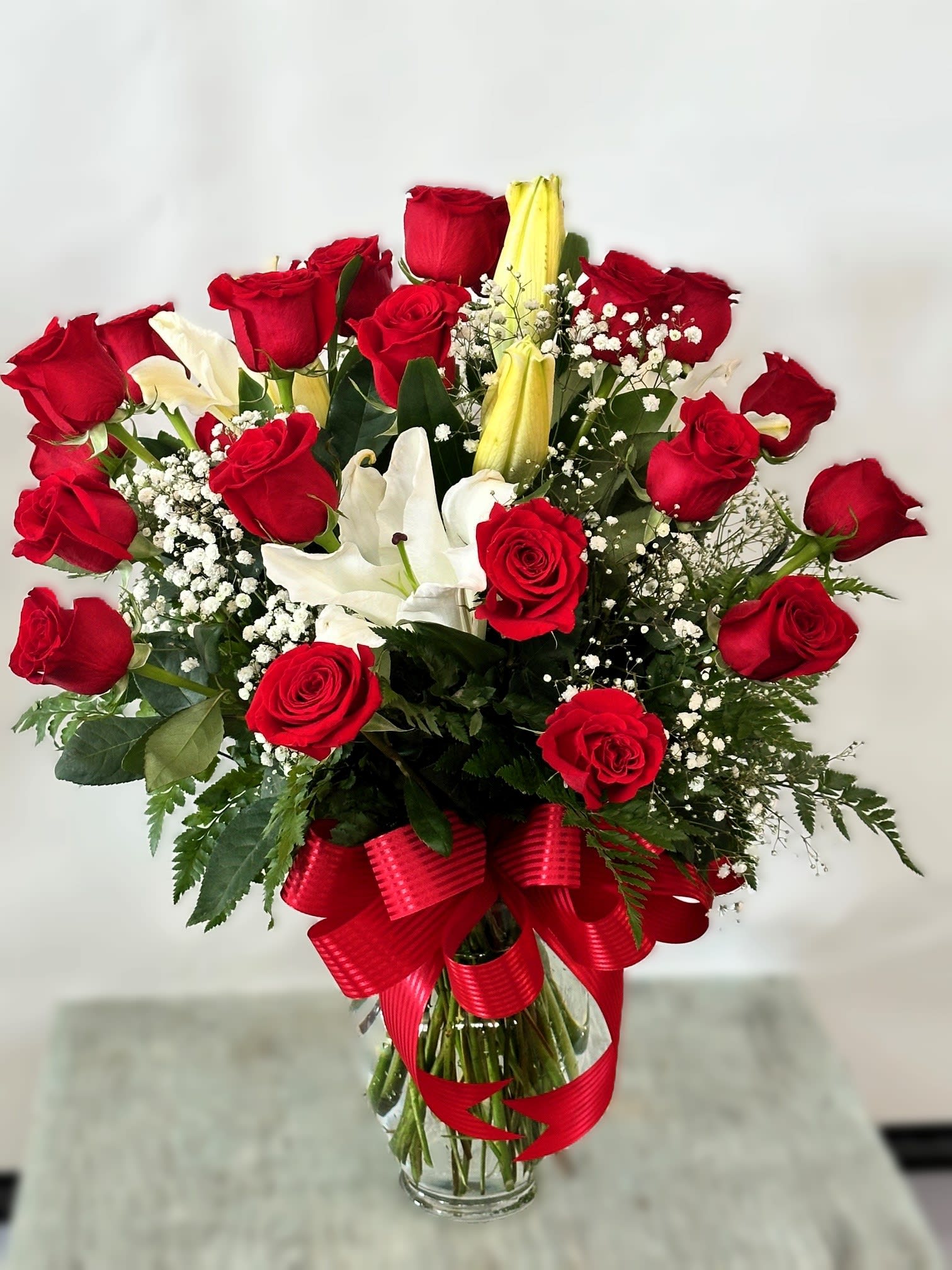 Red roses and white lilies in a clear glass vase with a red ribbon