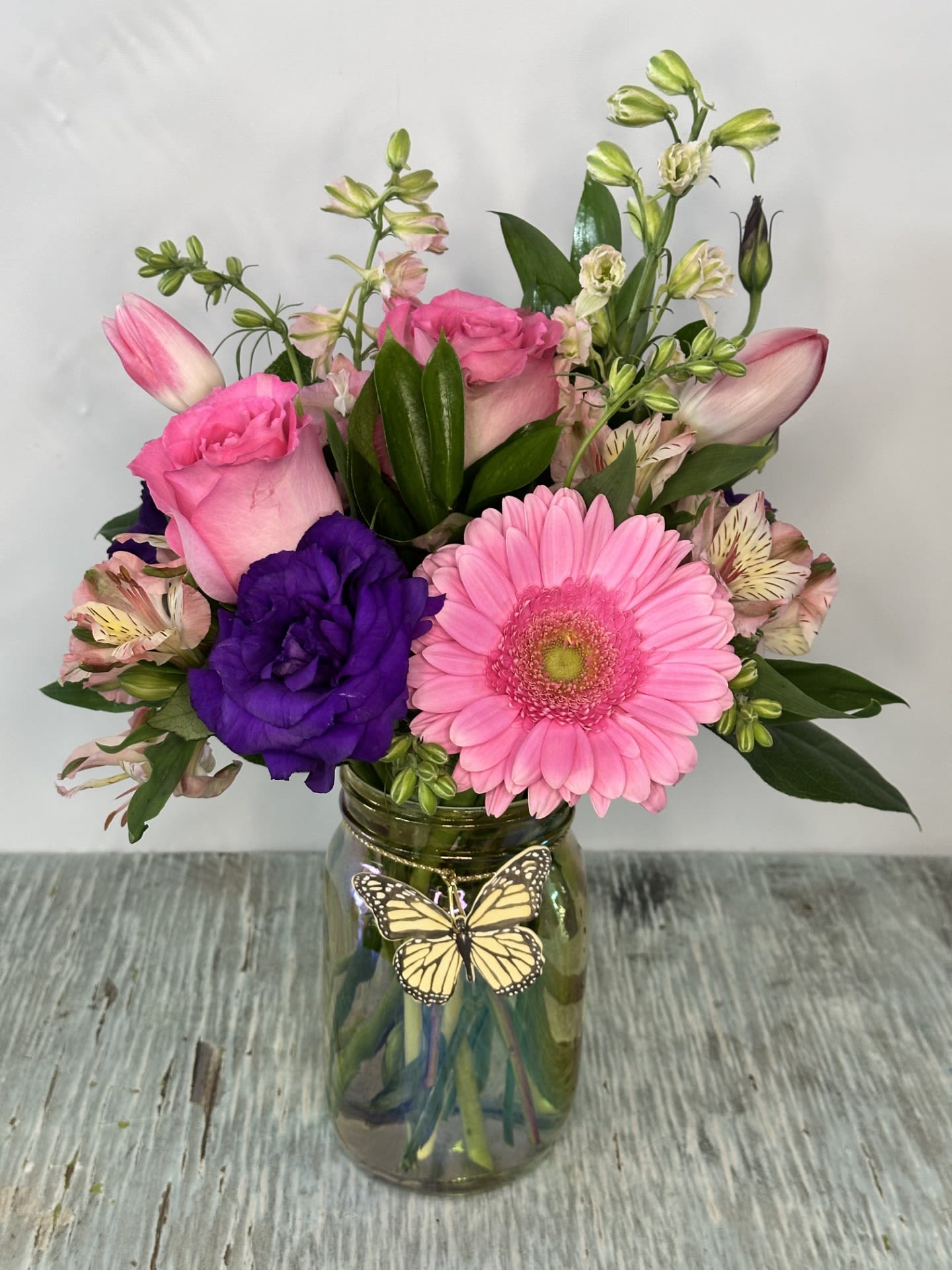 Pink and purple mixed bouquet in a glass jar with a butterfly decoration