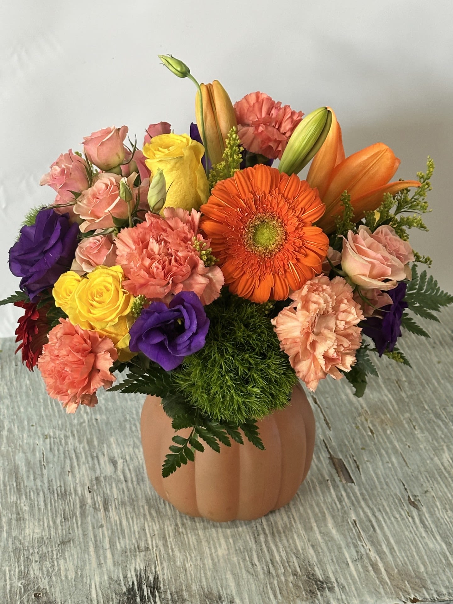 Mixed bouquet in a pumpkin-shaped vase with orange, pink, purple, and yellow flowers
