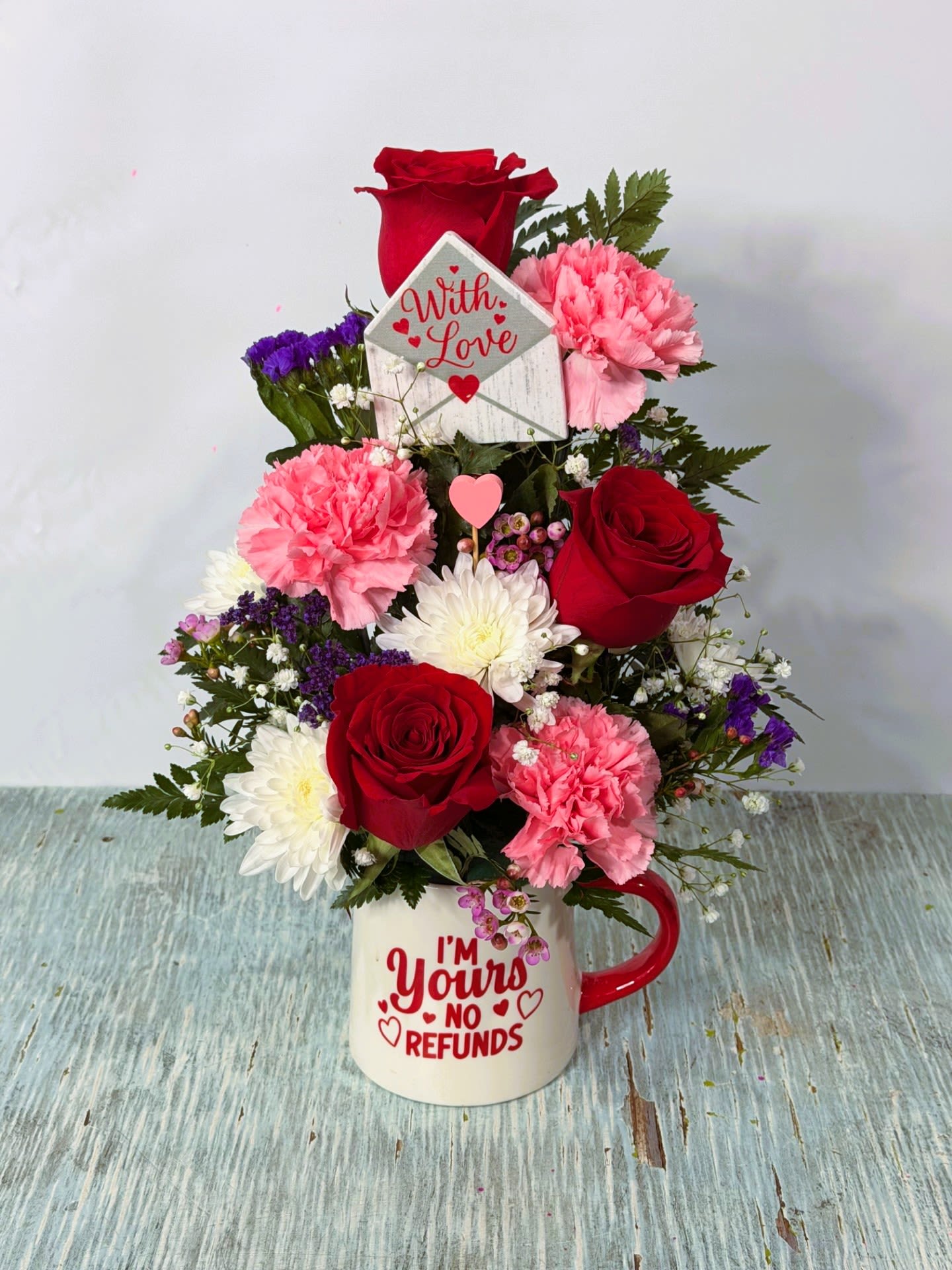 Bouquet of red roses, pink carnations, and white daisies in a mug