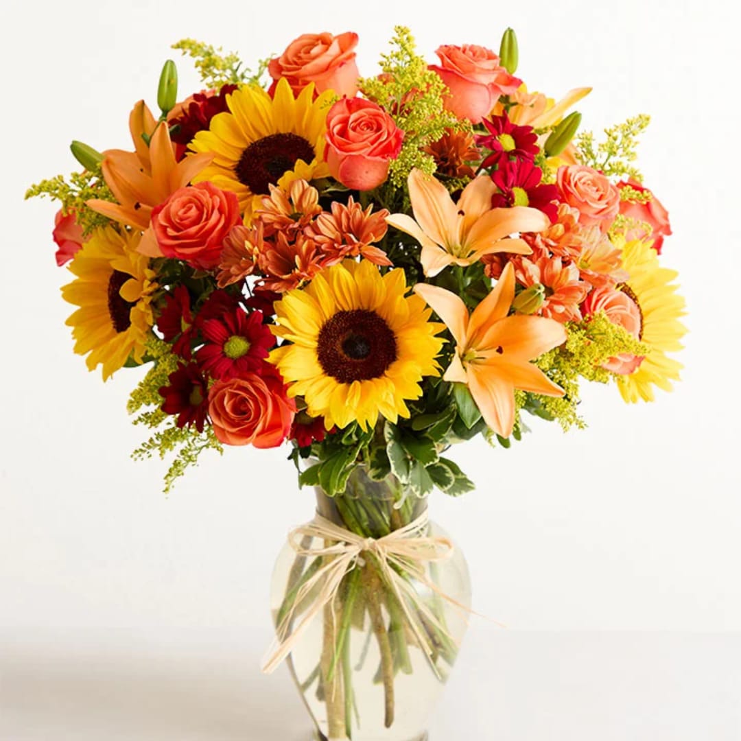Mixed bouquet of sunflowers, roses, lilies, and daisies in a glass vase