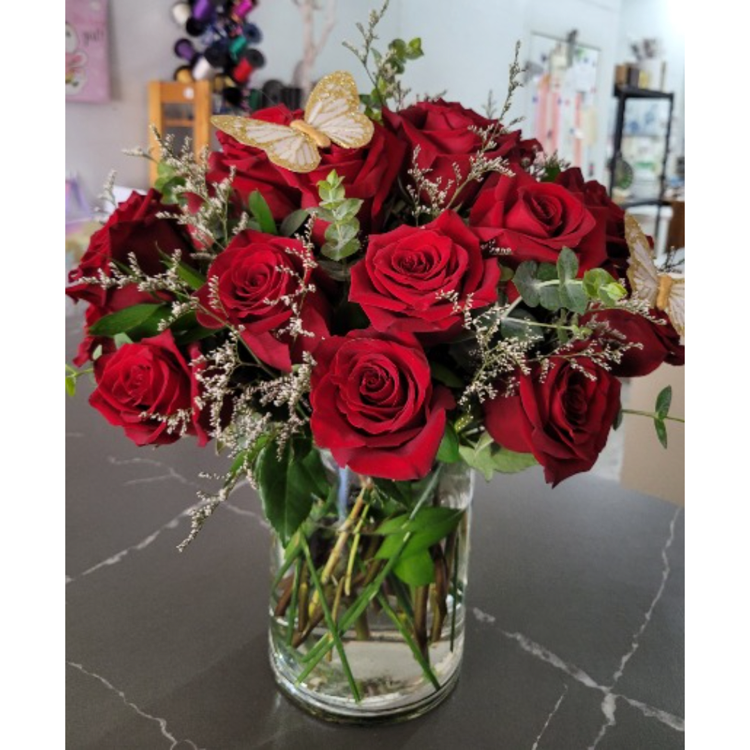 Red roses arranged in a clear glass vase with a butterfly accent