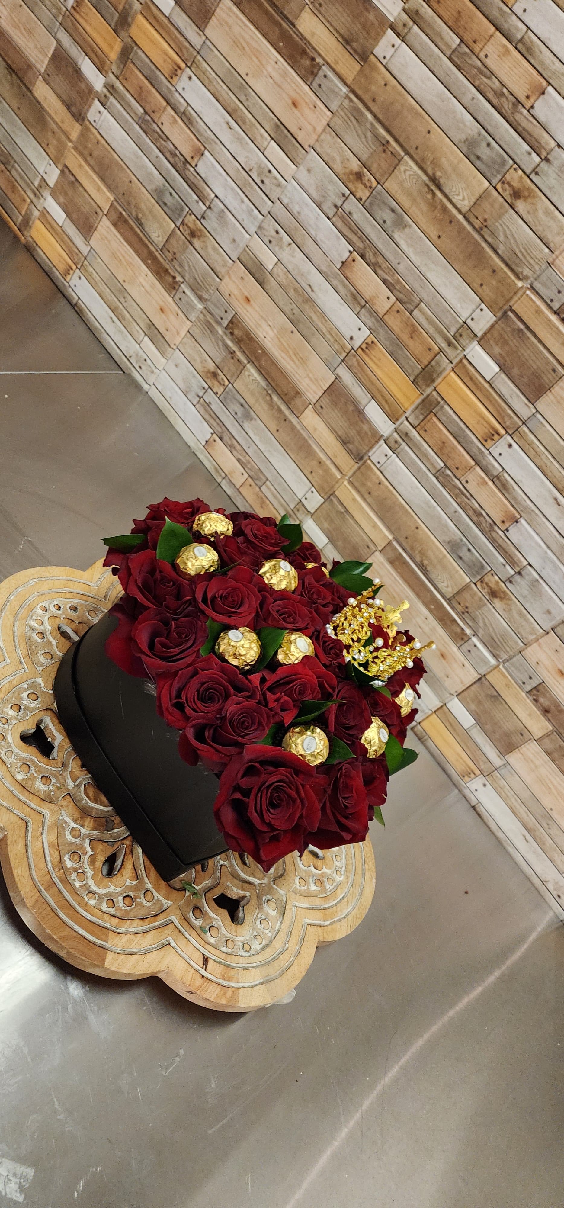 Red roses in a black box with gold chocolates and a crown topper