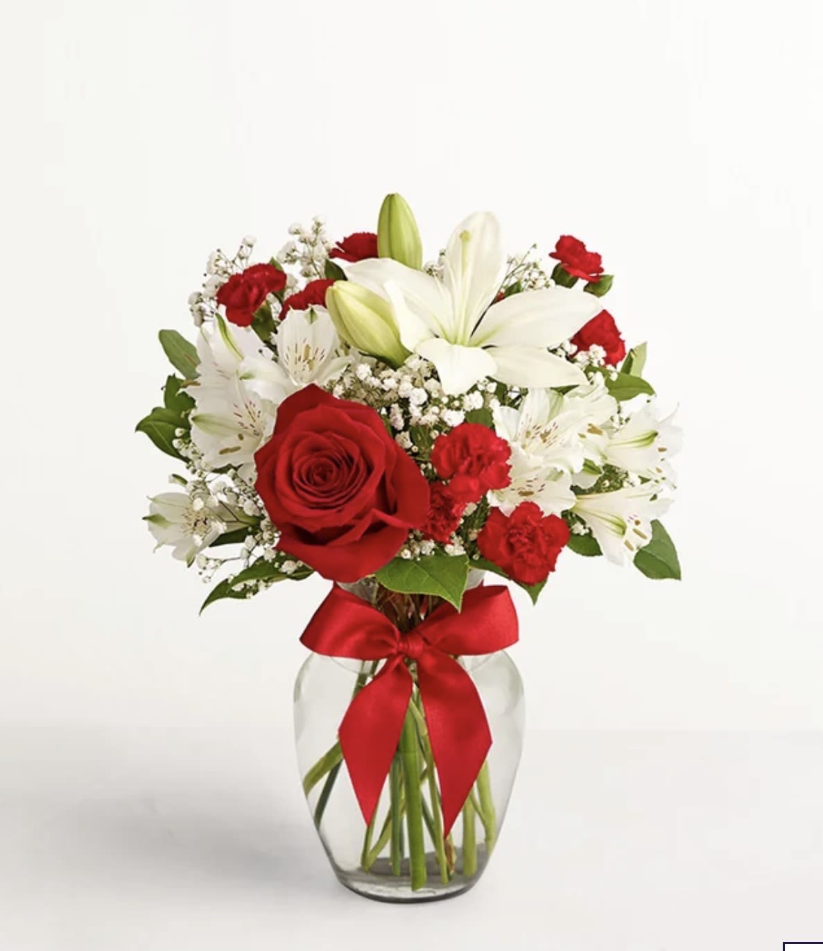 Red roses and white lilies arranged in a glass vase with a red ribbon