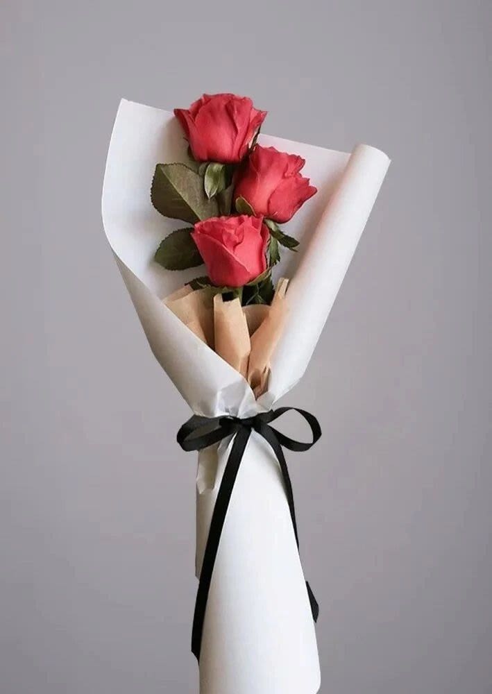 Three red roses wrapped in white paper with a black ribbon