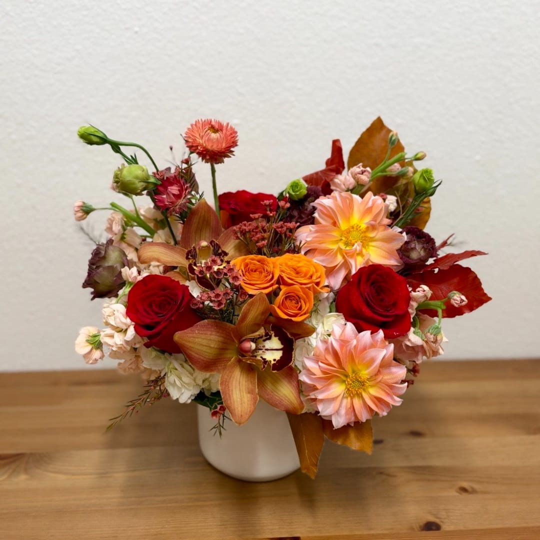 Mixed bouquet of red, peach, and orange flowers in a white vase