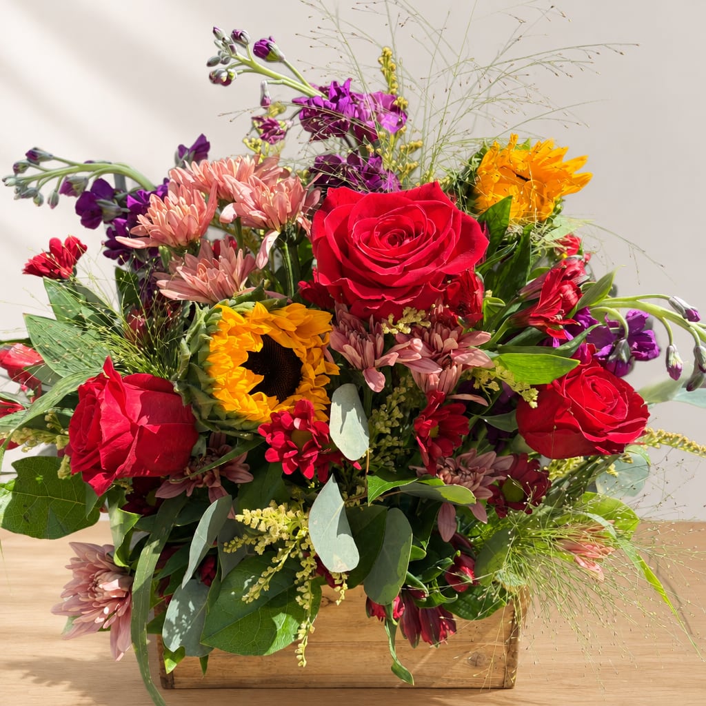 Mixed bouquet with red roses, sunflowers, and pink daisies in a wooden box