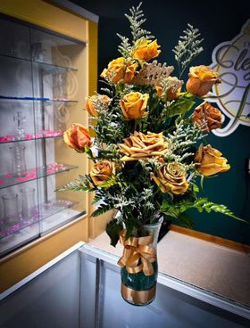 Tall bouquet of orange roses in a gold vase with a ribbon