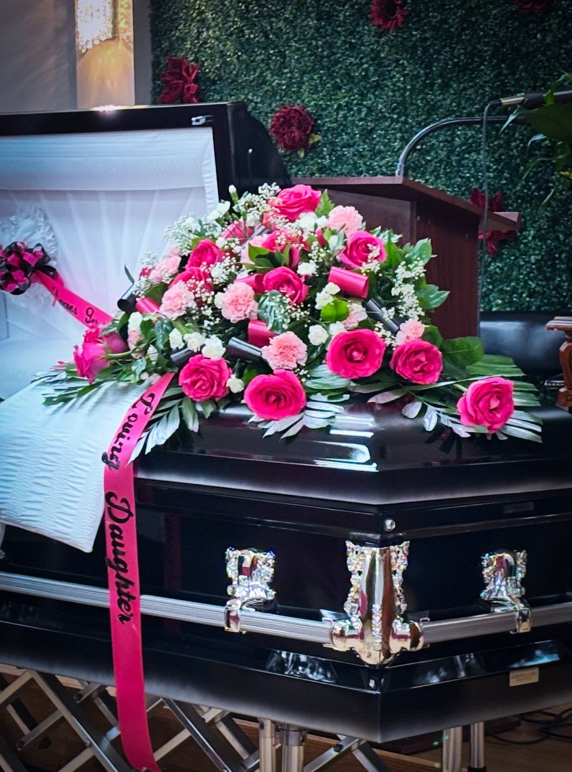 Pink rose and carnation casket spray with ribbon on a black casket
