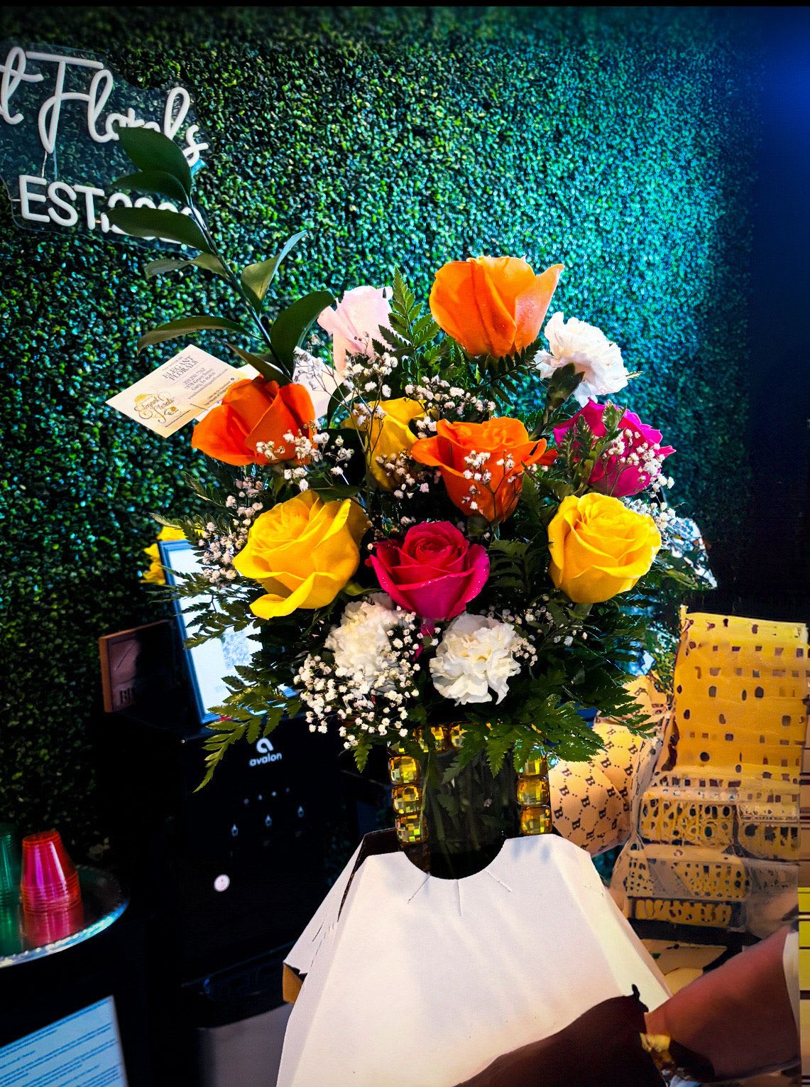 Bright Mixed Rose Vase Arrangement - This vibrant arrangement features a joyful mix of orange, yellow, pink, and white roses, accented with soft white carnations, baby’s breath, and fresh greenery. Designed in a clear glass vase, this colorful bouquet radiates happiness, warmth, and celebration. Perfect for birthdays, congratulations, get-well wishes, or simply to brighten someone’s day, this arrangement brings a burst of color and positivity to any space.  Flower colors and varieties may vary slightly due to seasonal availability while maintaining the overall look and style.