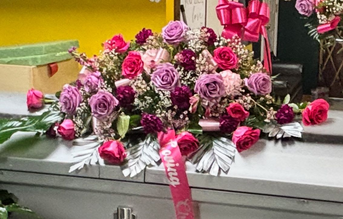 Pink and lavender rose arrangement on a casket with ribbon accents