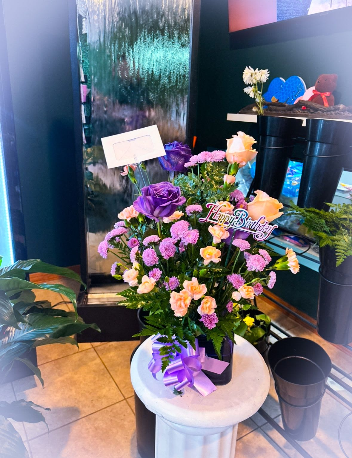 Purple and peach flower arrangement with a Happy Birthday sign in a black container