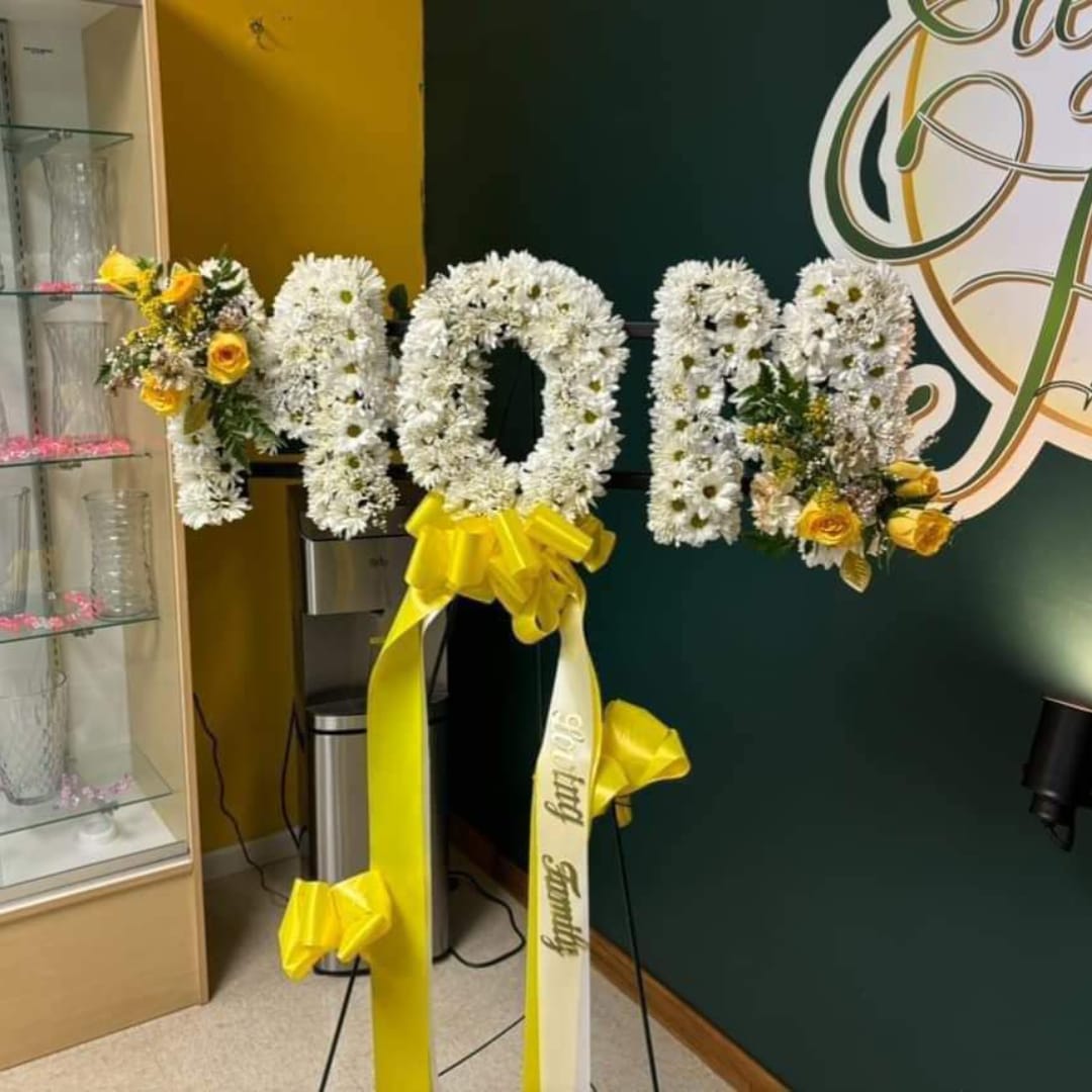 White floral letters on a stand with yellow ribbon accents