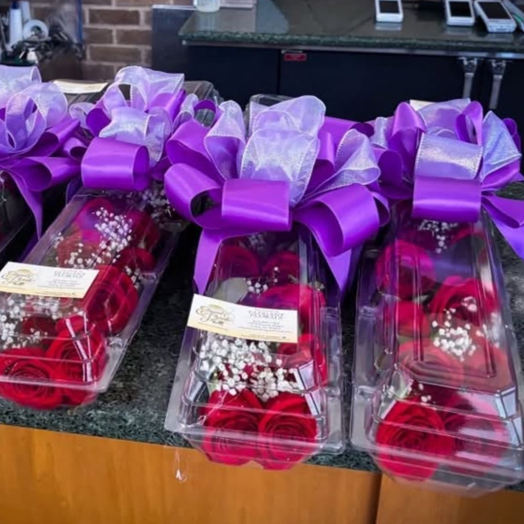 Three boxed rose arrangements with purple bows and clear lids