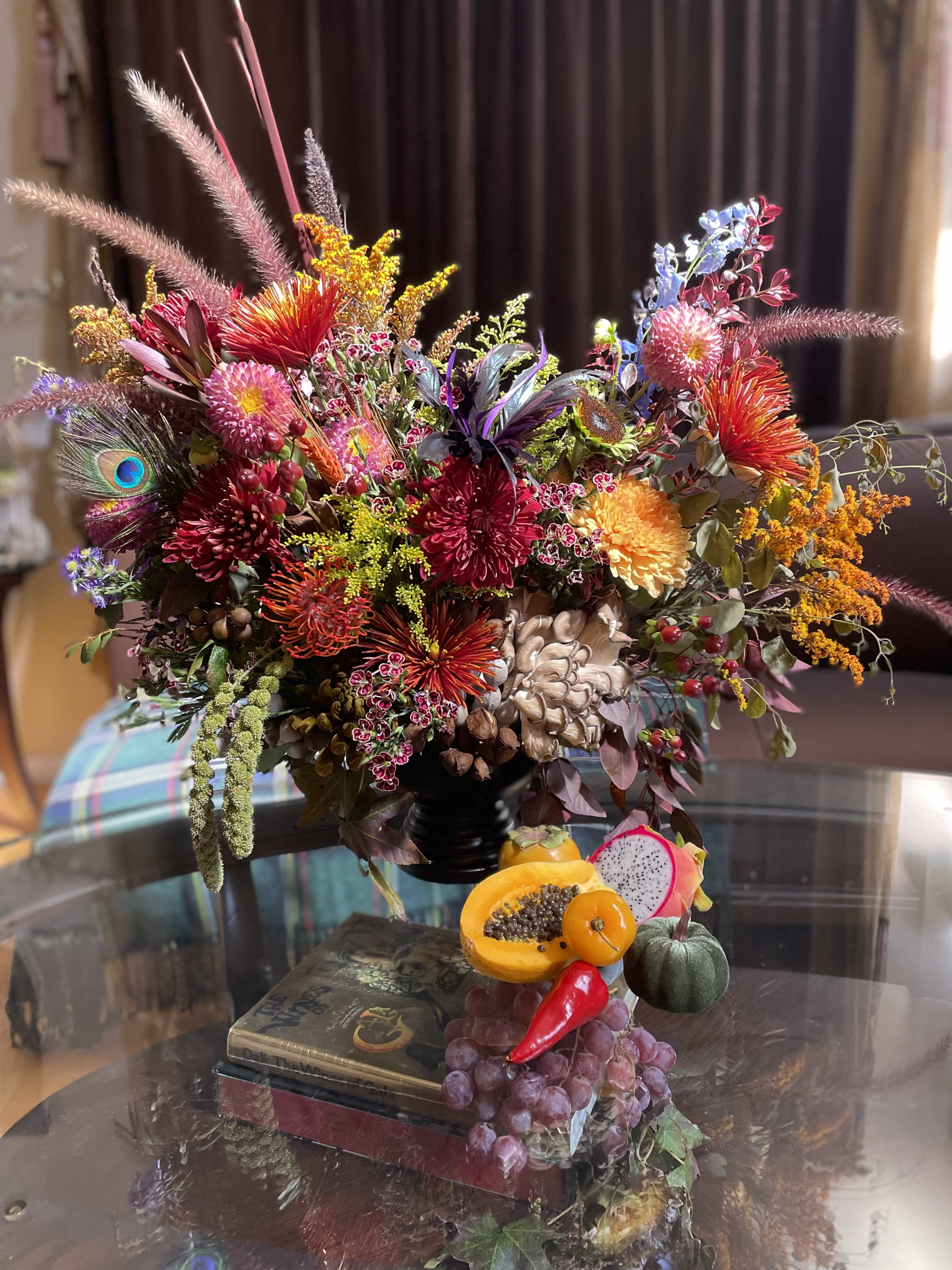 Colorful mixed floral arrangement with fruit accents in a dark vase