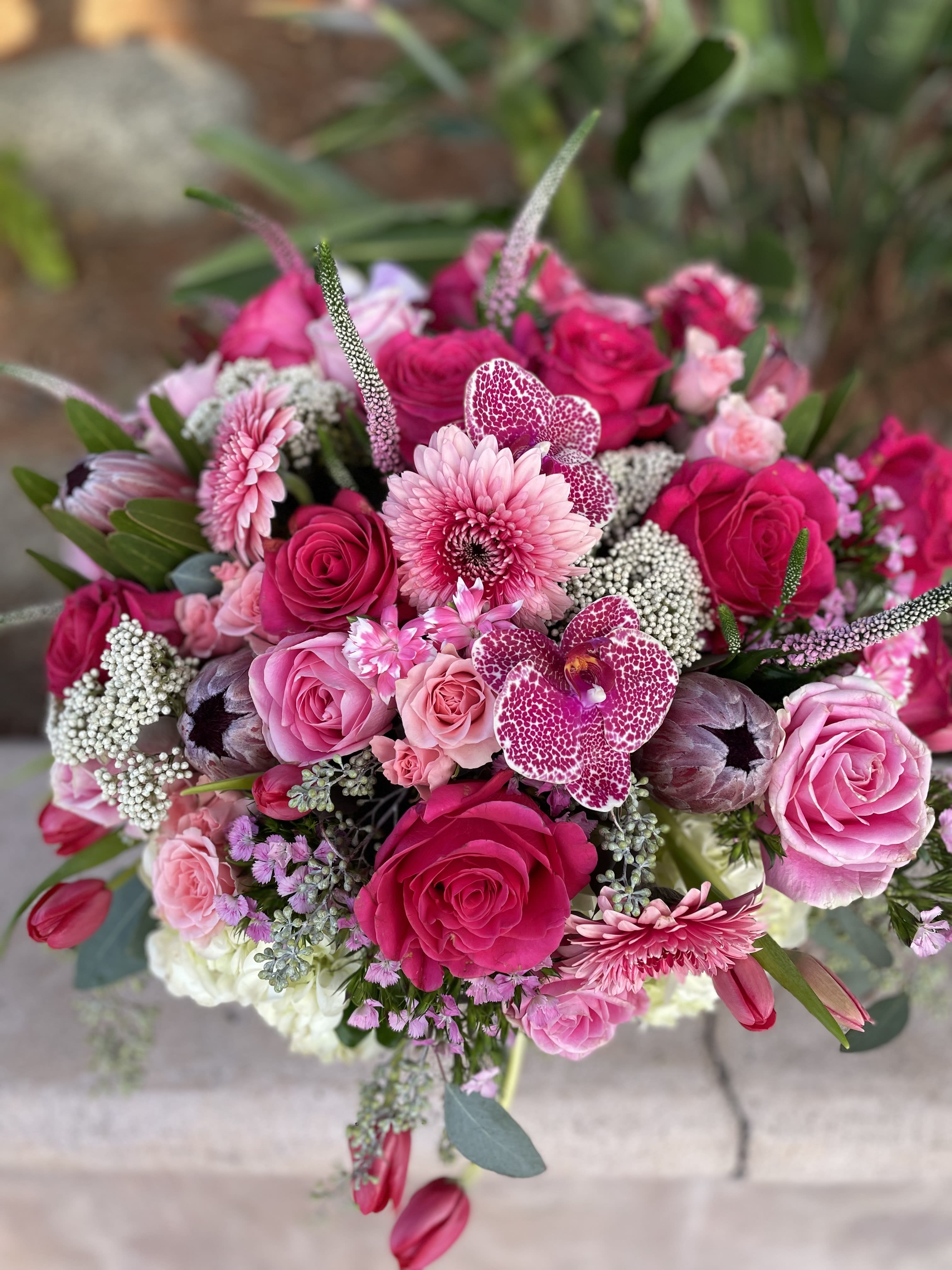 Pink and magenta bouquet with roses, orchids, and daisies